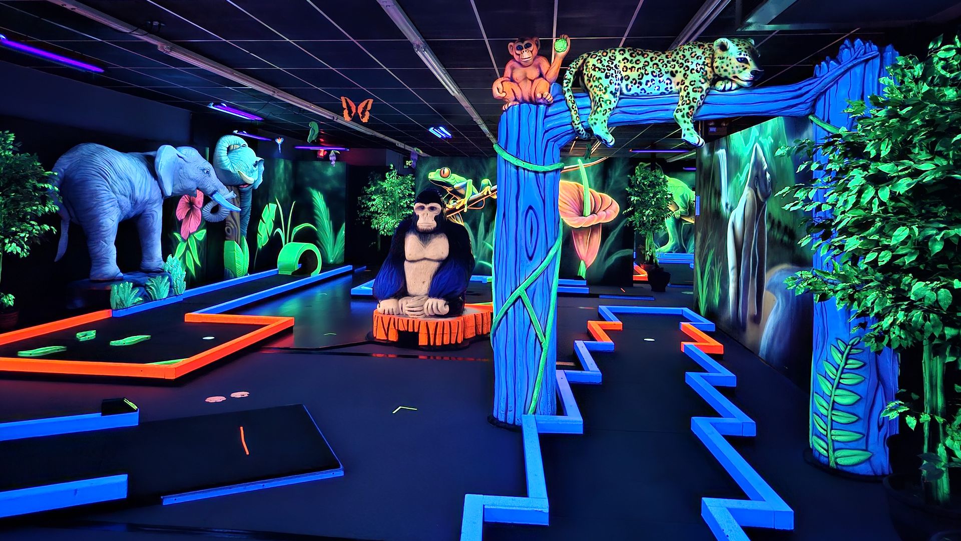 A neon putt-putt course under black lights, with a leopard lounging on a branch and a gorilla and elephants in the background
