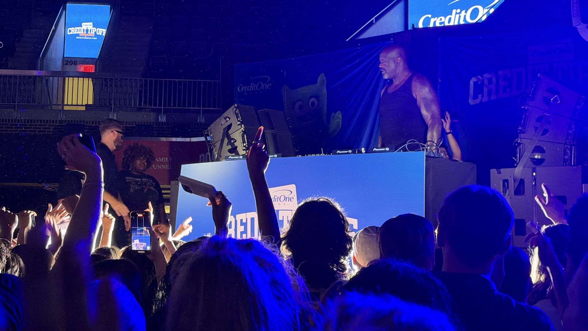 A crowded concert scene bathed in deep blue light as Shaquille O'Neal performs at the booth.