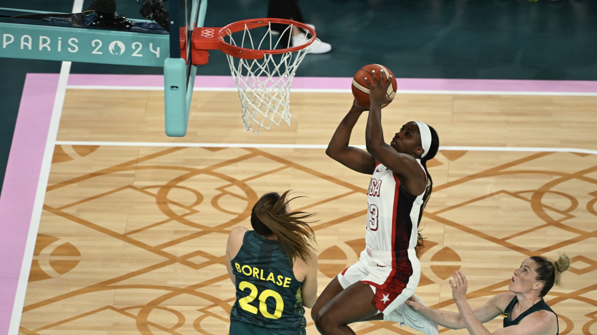 A U.S. women's basketball player shoots near the trim among two Australian players.