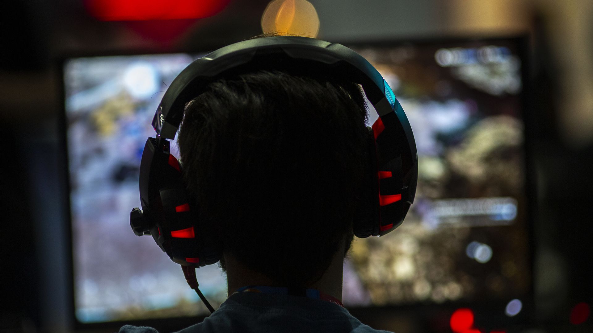 Photo of a silhouetted person's head, wearing headphones, as they gaze at a blurred screen