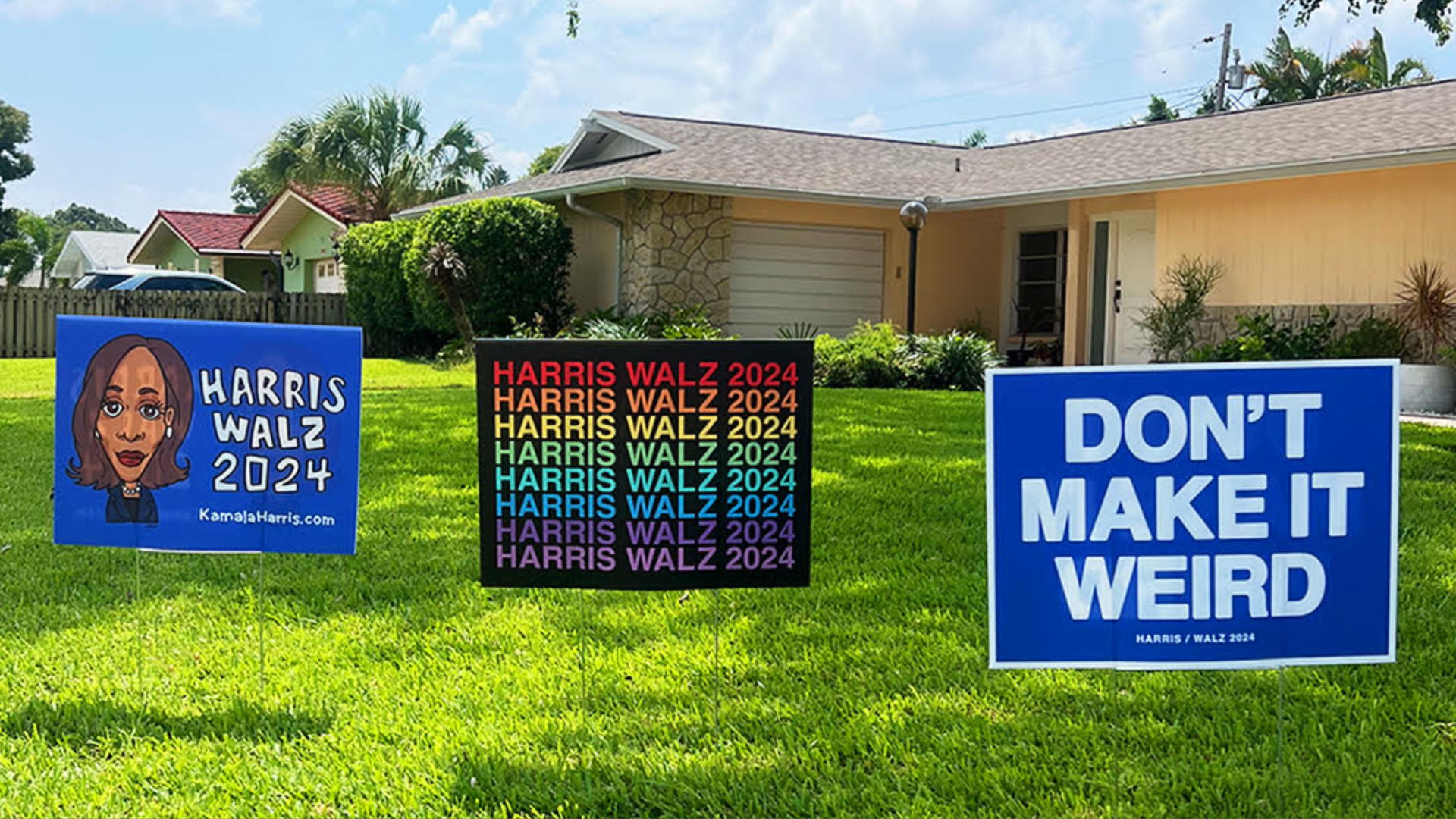 Three political campaign signs sitting in the front yard of a light orange-colored home. The sign on the left says "Harris Walz 2024" beside a drawing of Vice President Kamala Harris. The second says "Harris Walz 2024" in rainbow colors. The third says, "DON'T MAKE IT WEIRD Harris/Walz 2024."