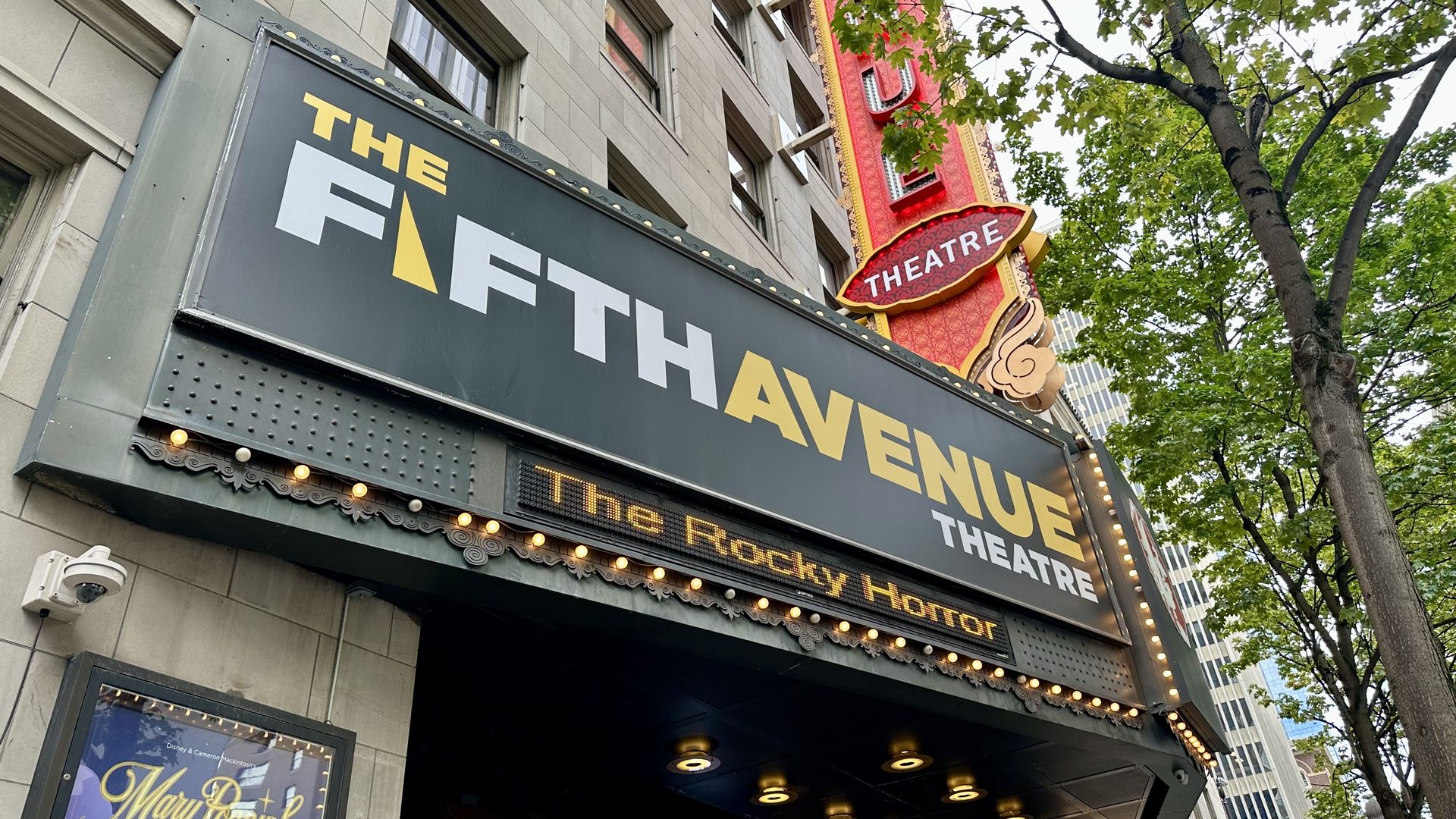 The marquee of the Fifth Avenue Theatre has the theater name in white and black capital letters, with "the Rocky Horror" digital letters sliding across the marquee. A red vertical sign with the theater name sits behind the marquee.