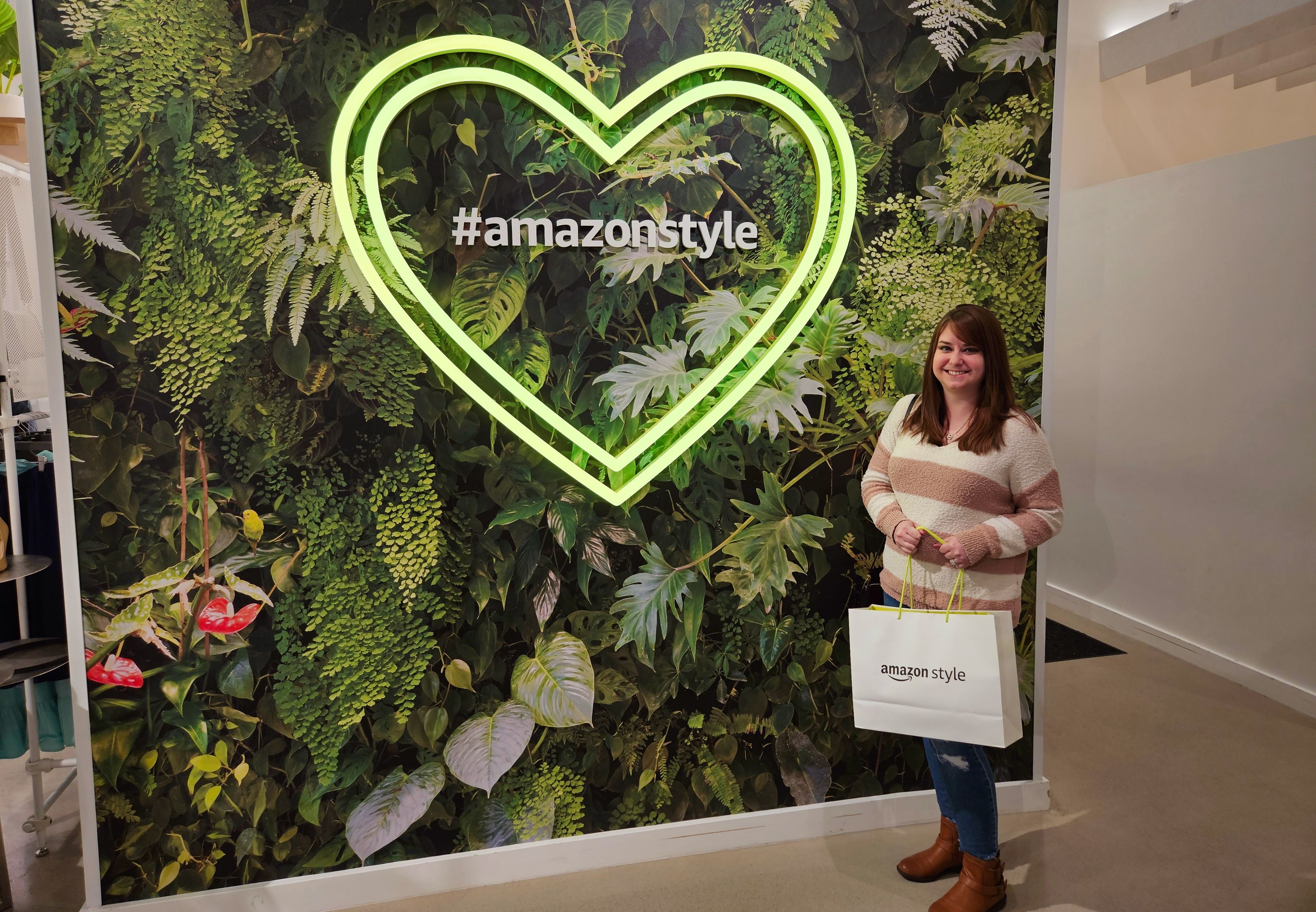 Alissa poses with a shopping bag next to a #amazonstyle sign with a neon heart light