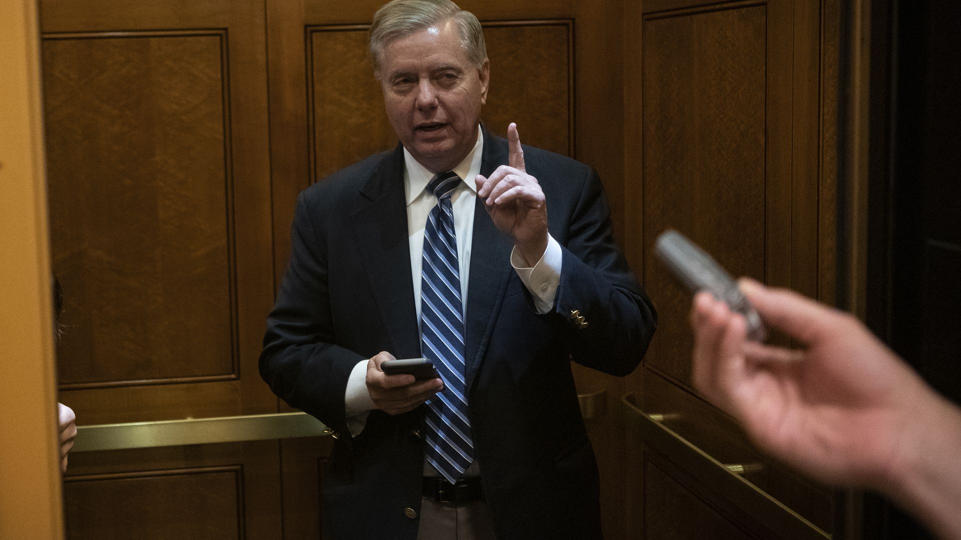 Photo of Sen. Lindsey Graham in an elevator with smartphone in one hand, and other hand's finger raised