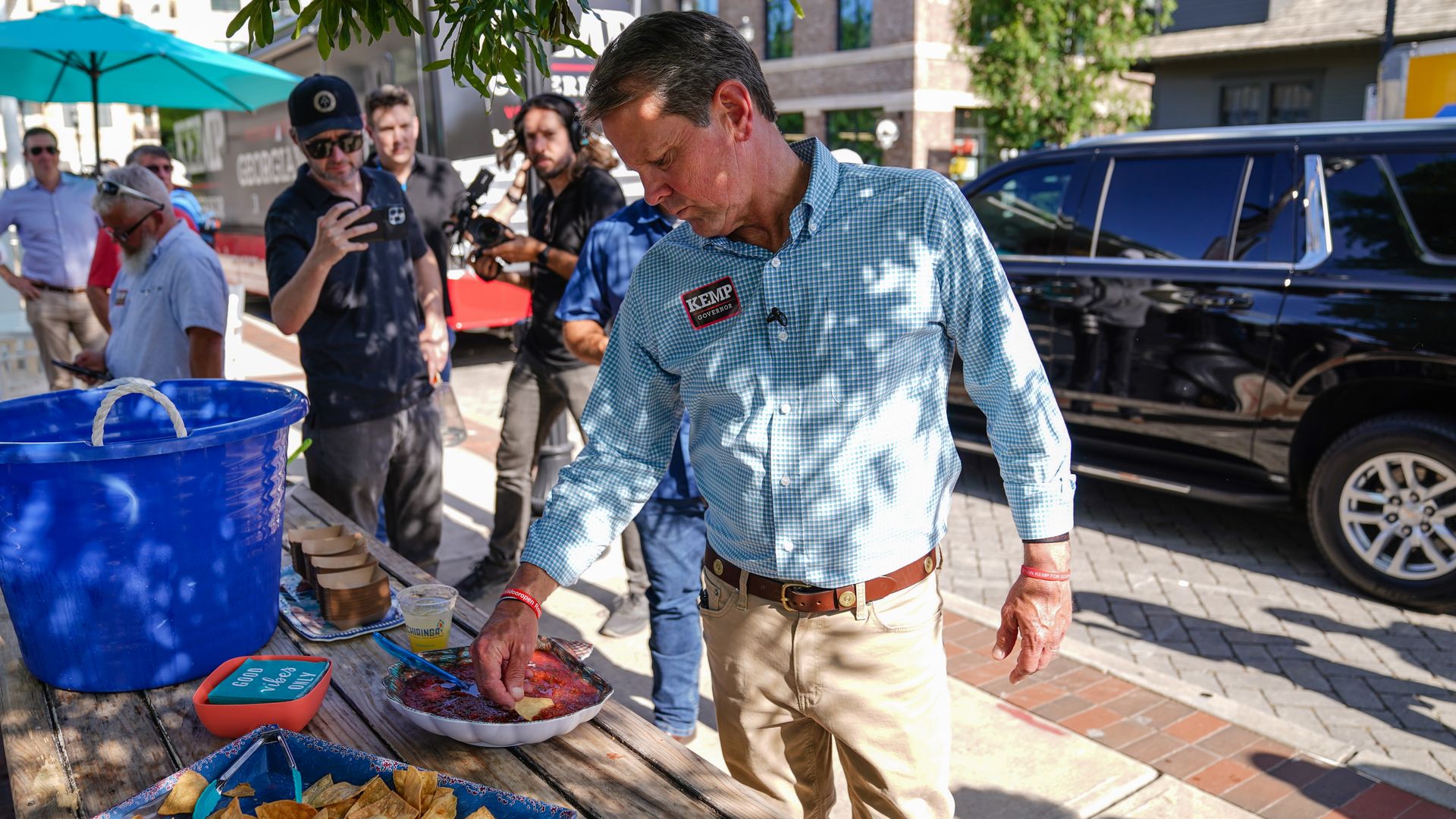 Gov. Brian Kemp dips a tortilla chip in salsa under the shade during a campaign stop in a mixed-use area 