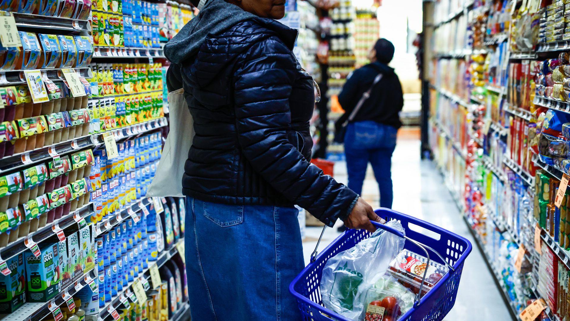 Shoppers hold grocery baskets filled with food in a store aisle 
