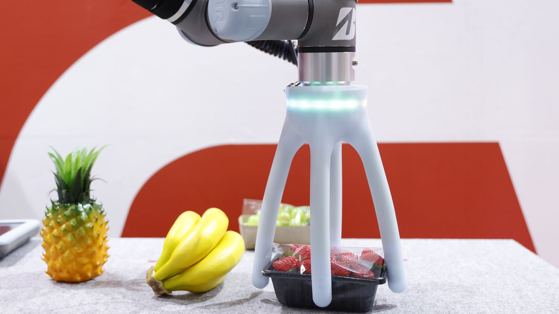A soft robotic hand grips a package of strawberries