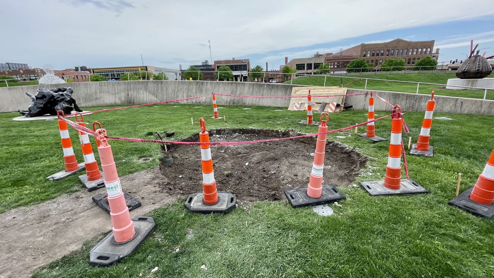 A photo of a dirt hole surrounded by traffic cones where the "Love" sculpture once stood in Des Moines' Pappajohn Sculpture Park.