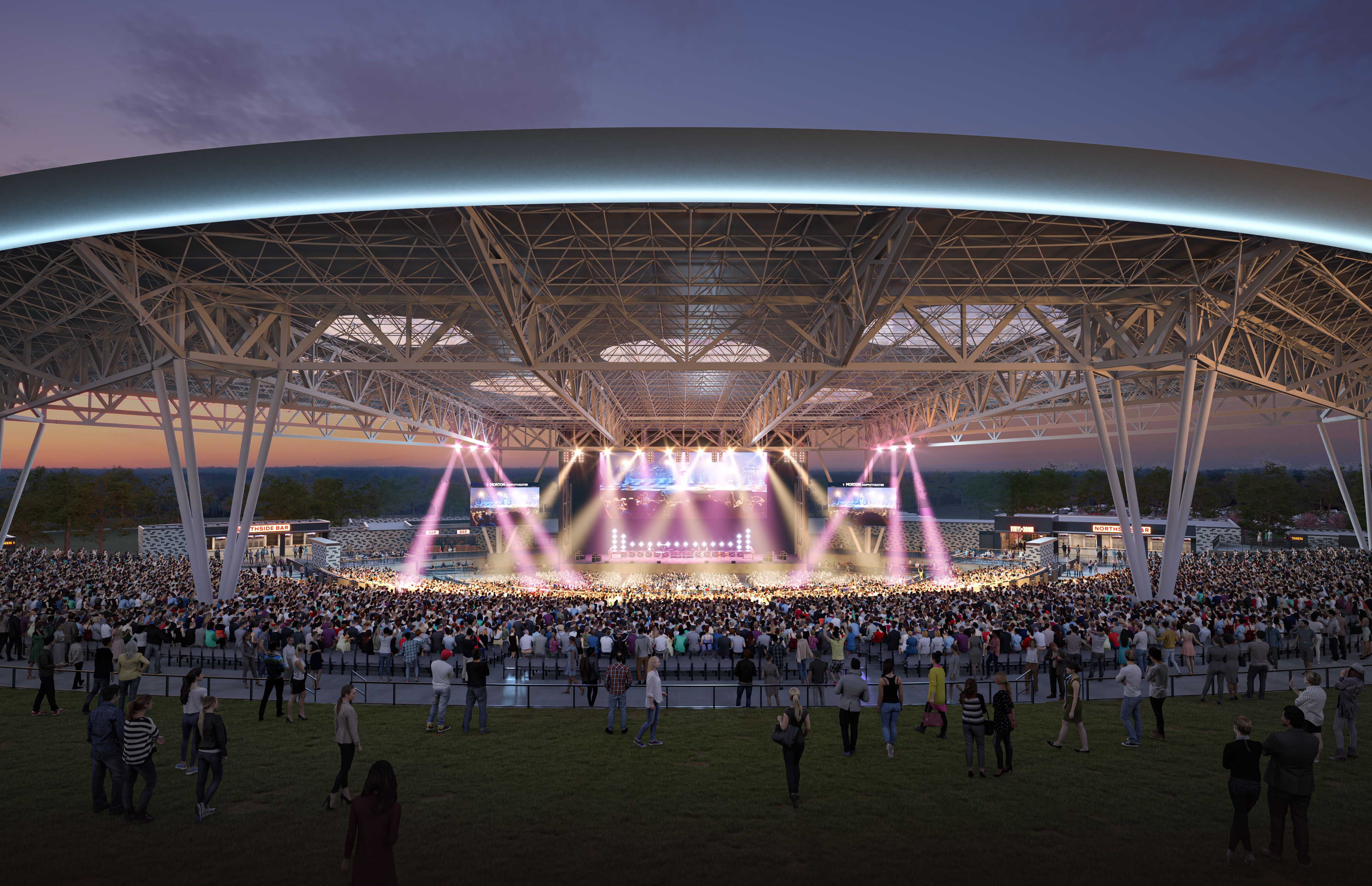 Large outdoor concert venue at dusk with a crowd facing a brightly lit stage under a curved roof with visible metal supports and pink spotlights.