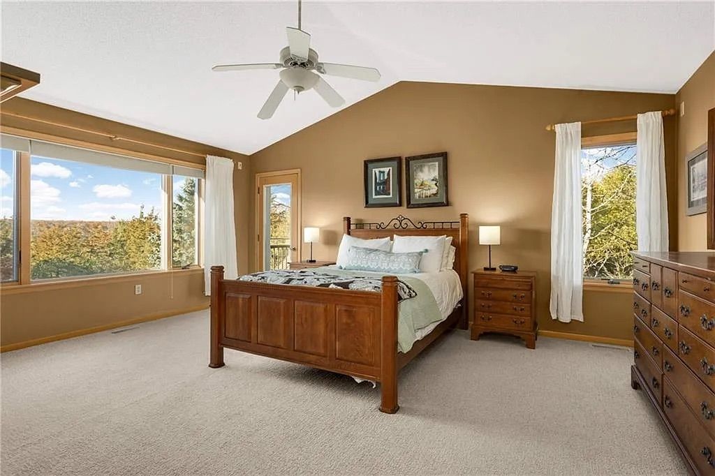 A master bedroom with beige walls, a large wood bed and windows showing a river.