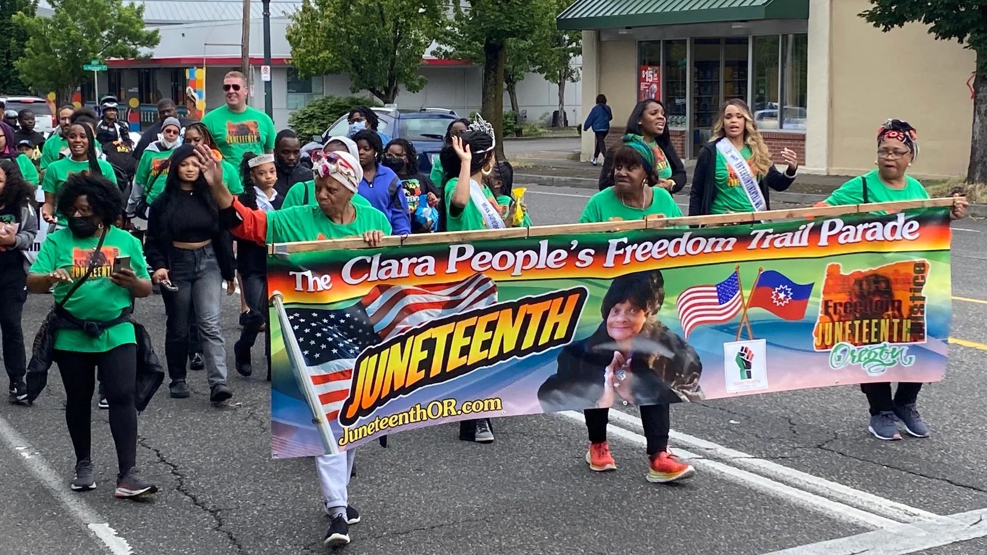 People marching in a parade, carrying a banner celebrating Juneteenth.