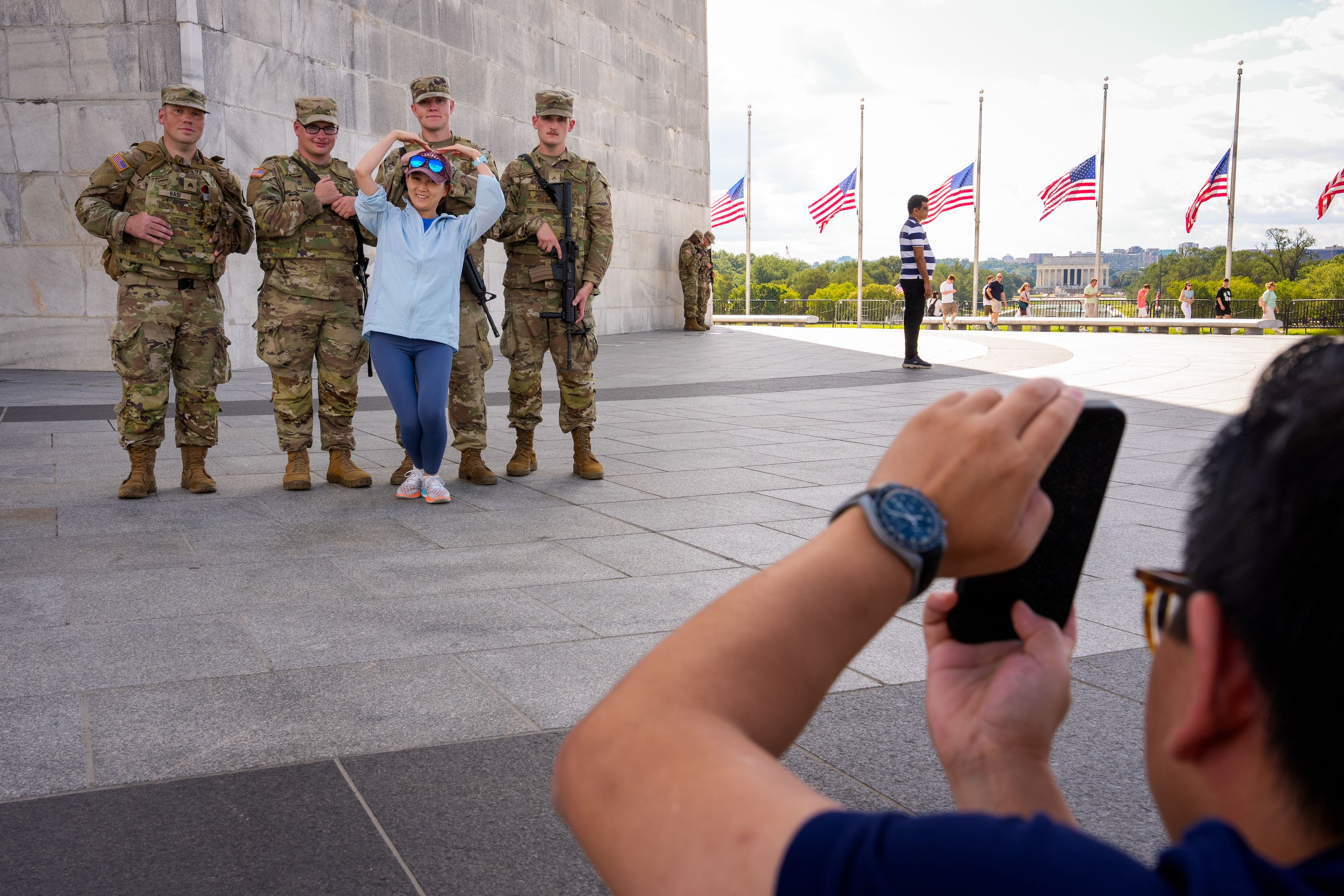A tourist visiting from Shenzhen, China, poses for a photograph with armed members of the National Guard at the base of the Washington on the National Mall on August 27, 2025 in Washington, DC. The Trump administration has deployed federal officers and the National Guard to the District in order to