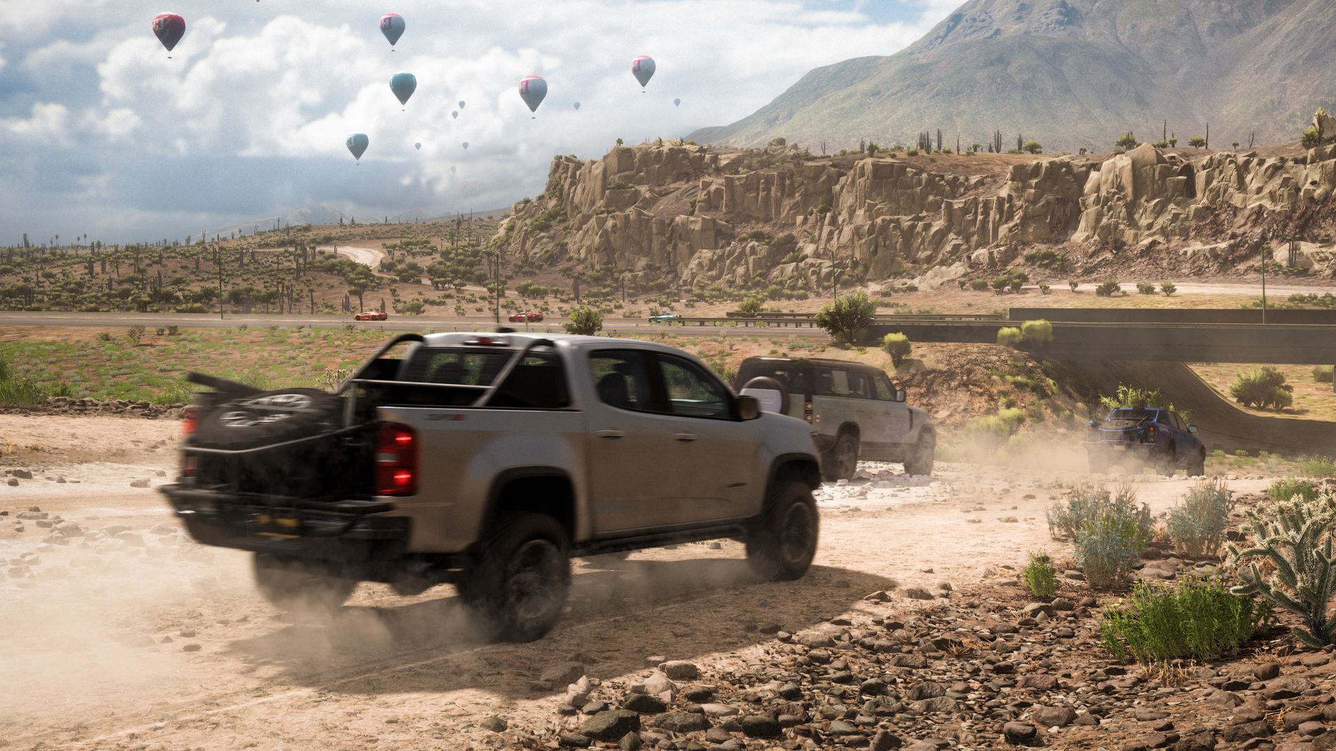 Screenshot of a jeep driving across a desert, as hot air balloons float overhead