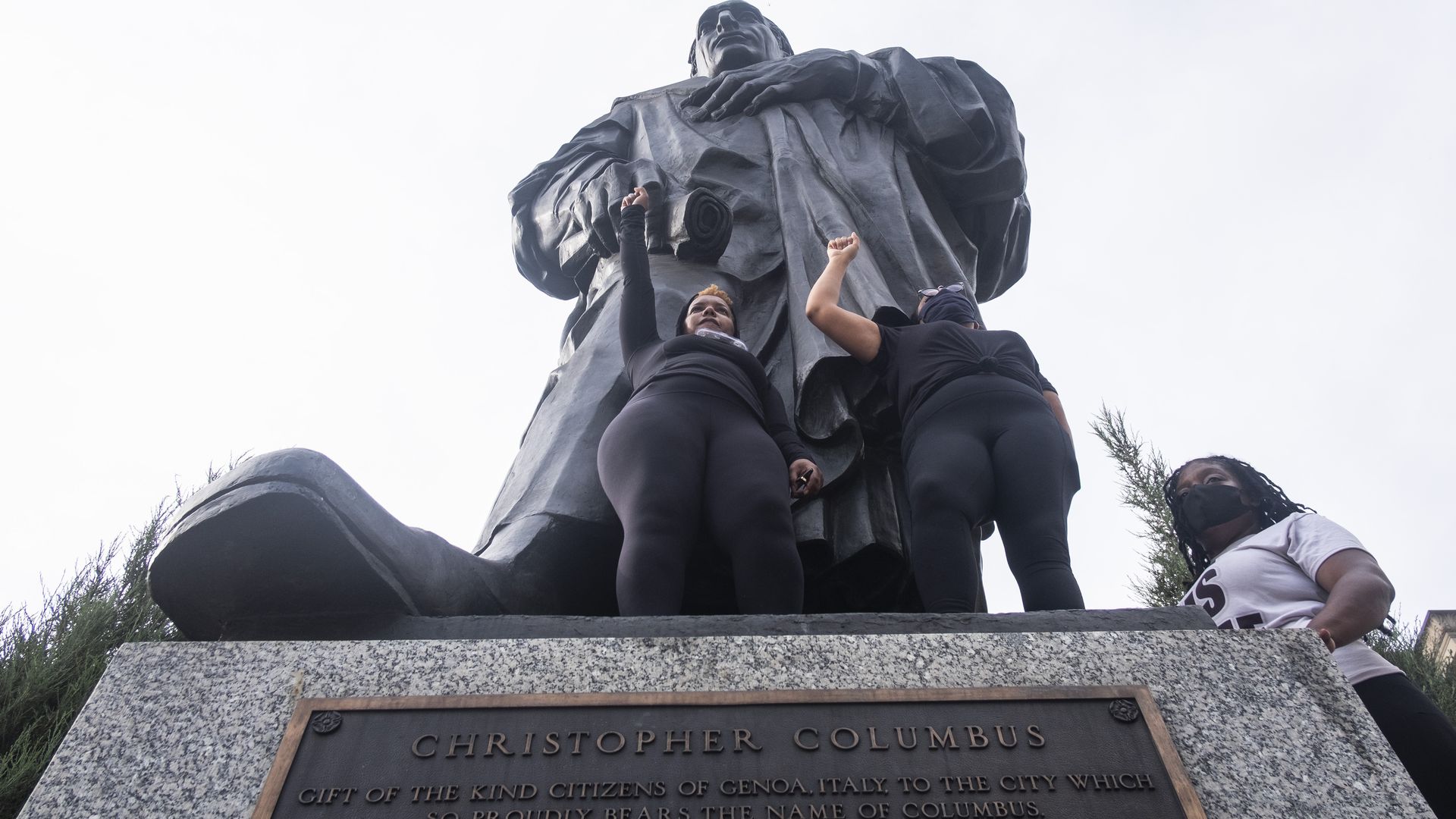 Protesters stand at the base of a Christopher Columbus statue.