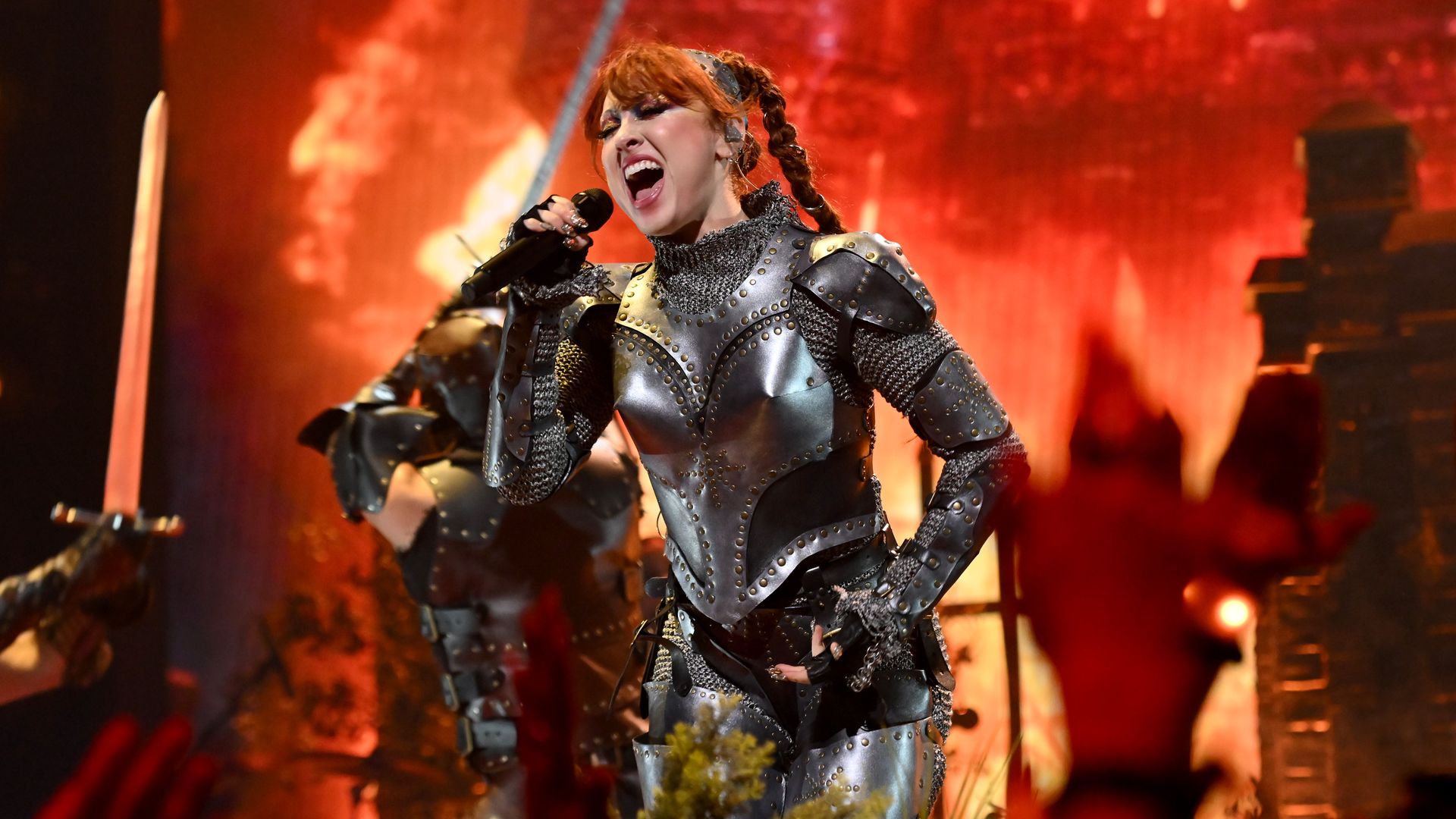 The singer Chappell Roan wearing a suit of armor costume and singing into a microphone.
