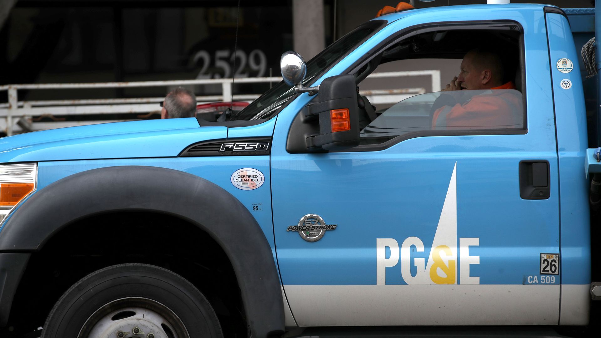 In this image, a man talks on the phone while driving a truck with the PG&E logo.