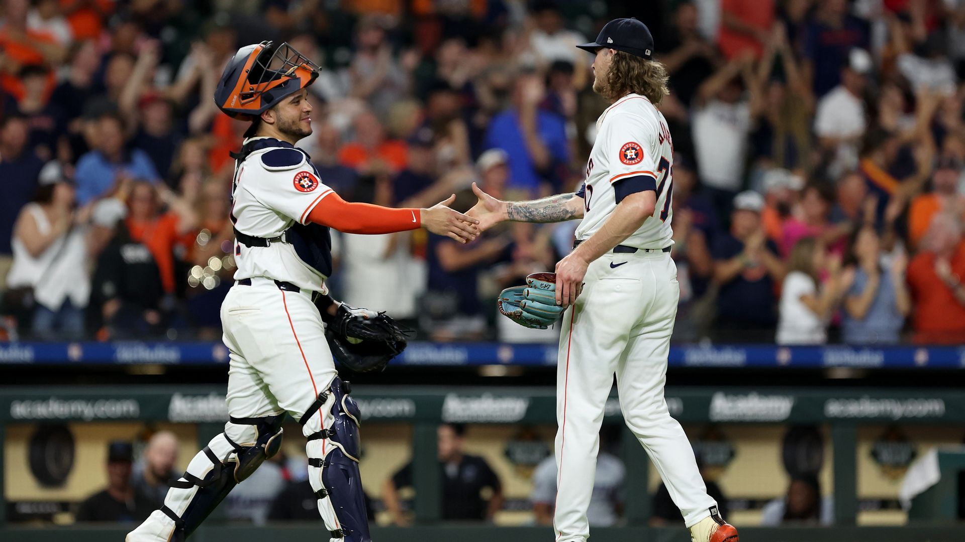 Two baseball players shake hands on the field in front of a crowd.
