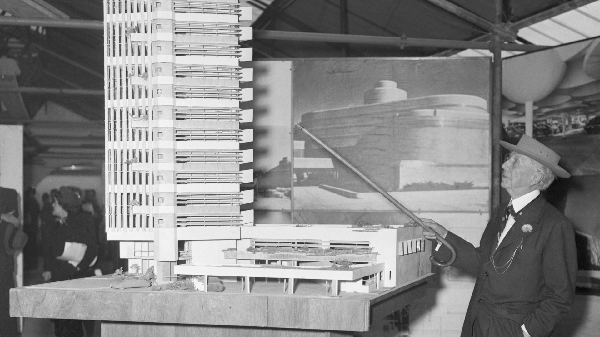 A black-and-white photo of Frank Lloyd Wright showing off a model of Price Tower