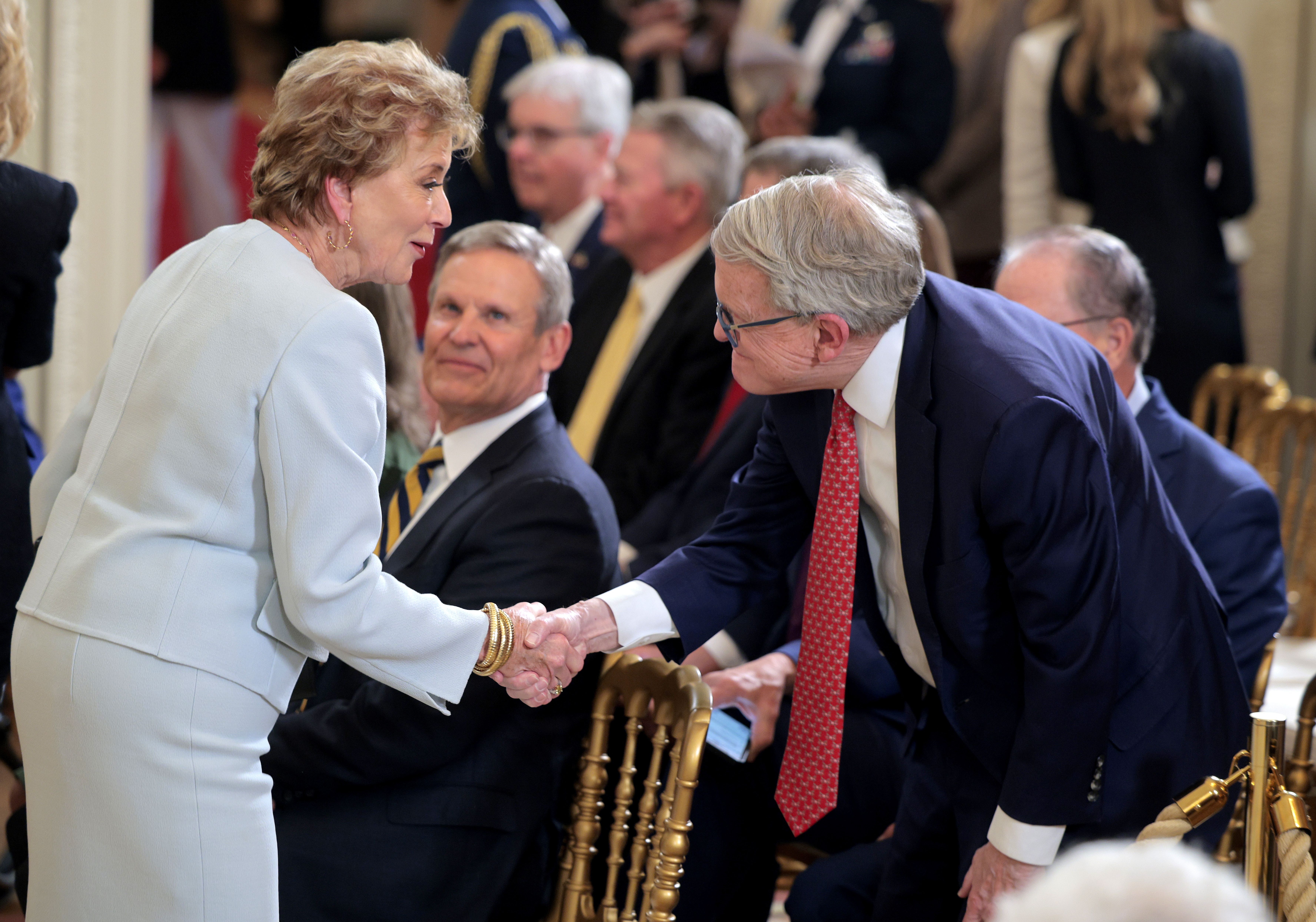 Secretary of Education Linda McMahon shakes hands with Ohio Gov. Mike DeWine in a room with seated people in formal attire.