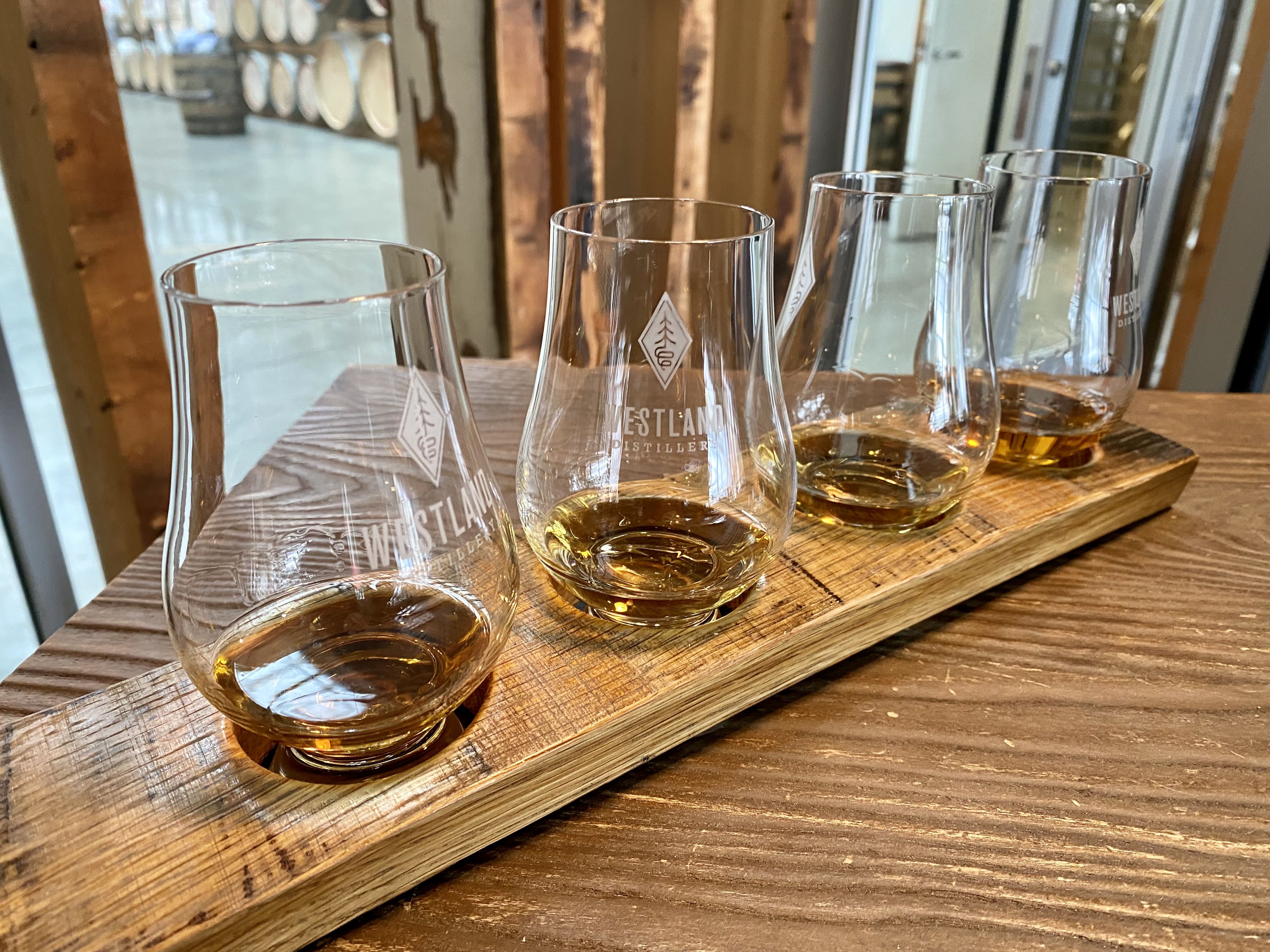 Four bell-shaped glasses of whiskey in a wooden holder on a wooden table. 