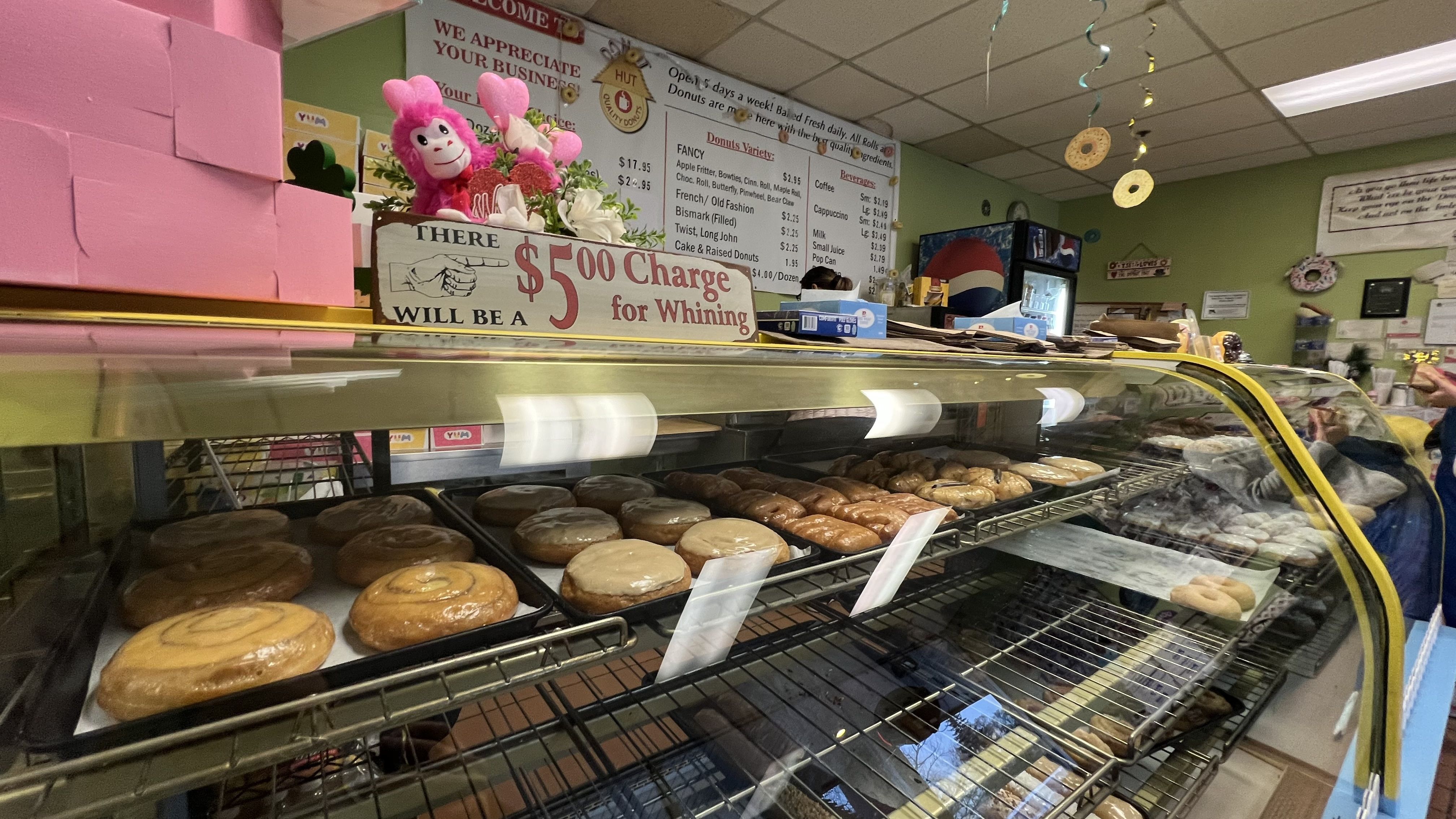 A display case at a donut shop with a sign reading "There Will Be A $5.00 Charge For Whining"