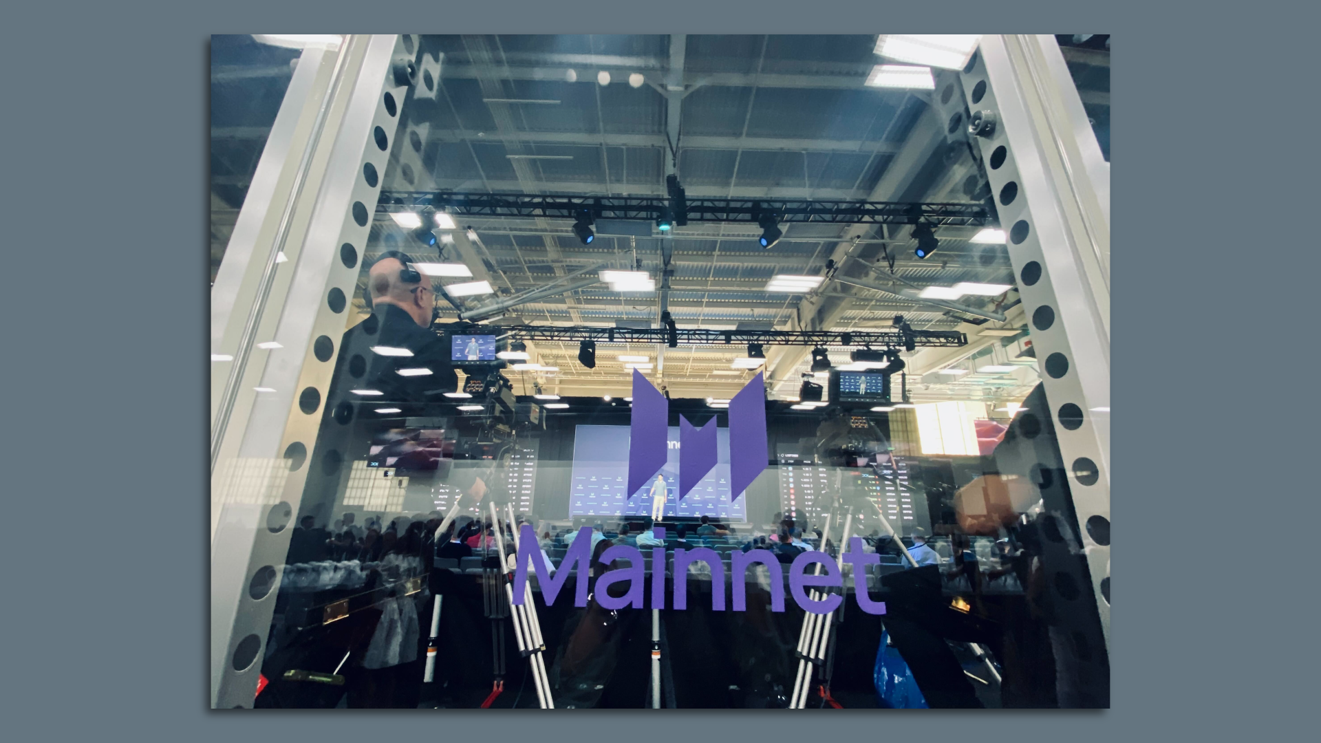 Mainnet logo on a window overlooking media equipment and a conference stage