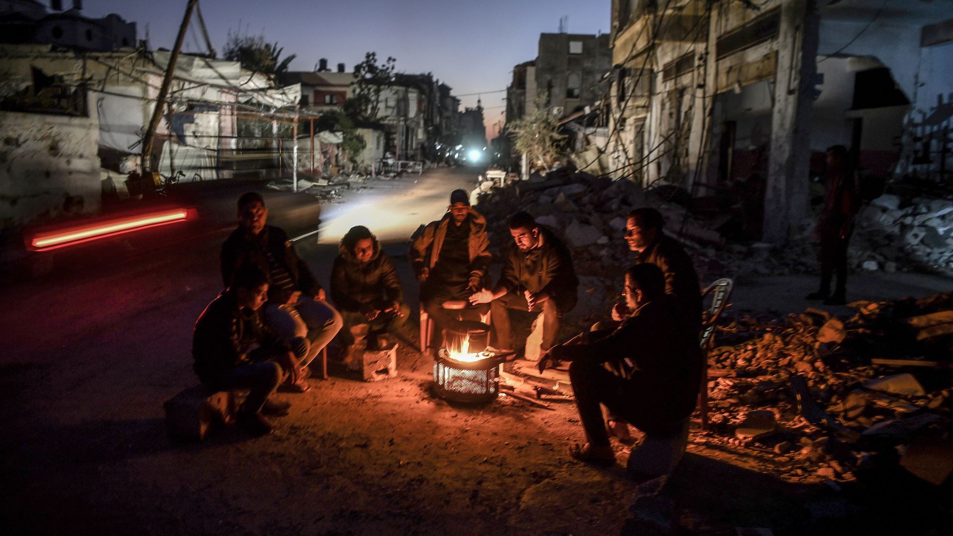 People gather around a fire near the rubble of a building in war-torn Gaza.