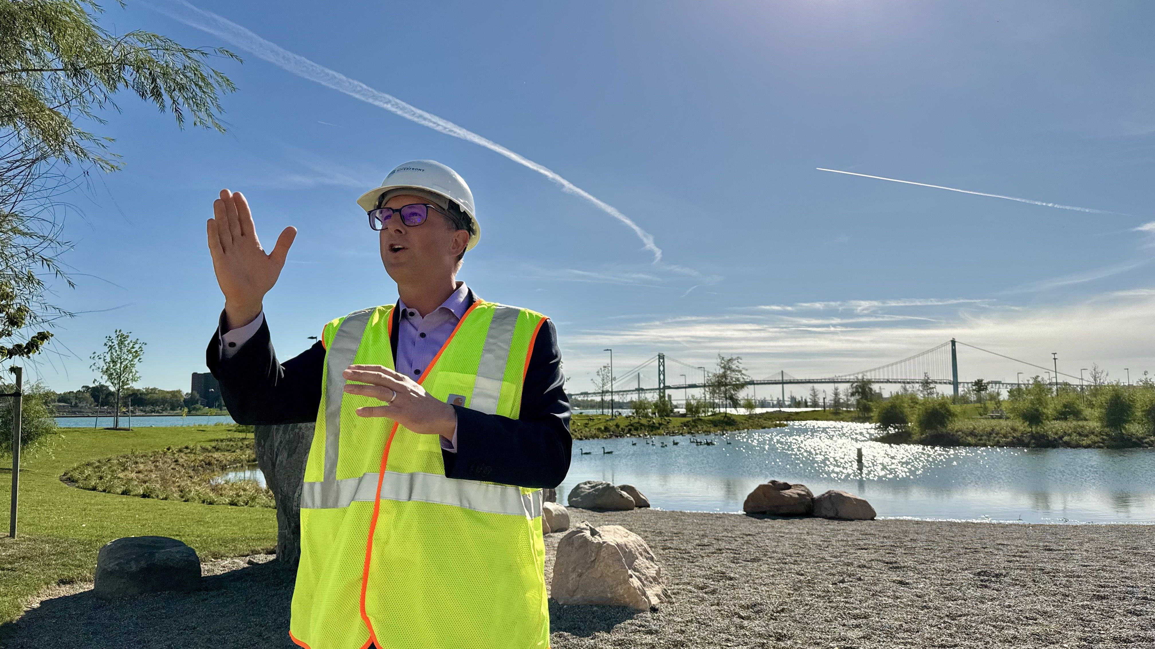 Ryan Sullivan gestures while speaking in front of the water garden with the riverfront view behind him.