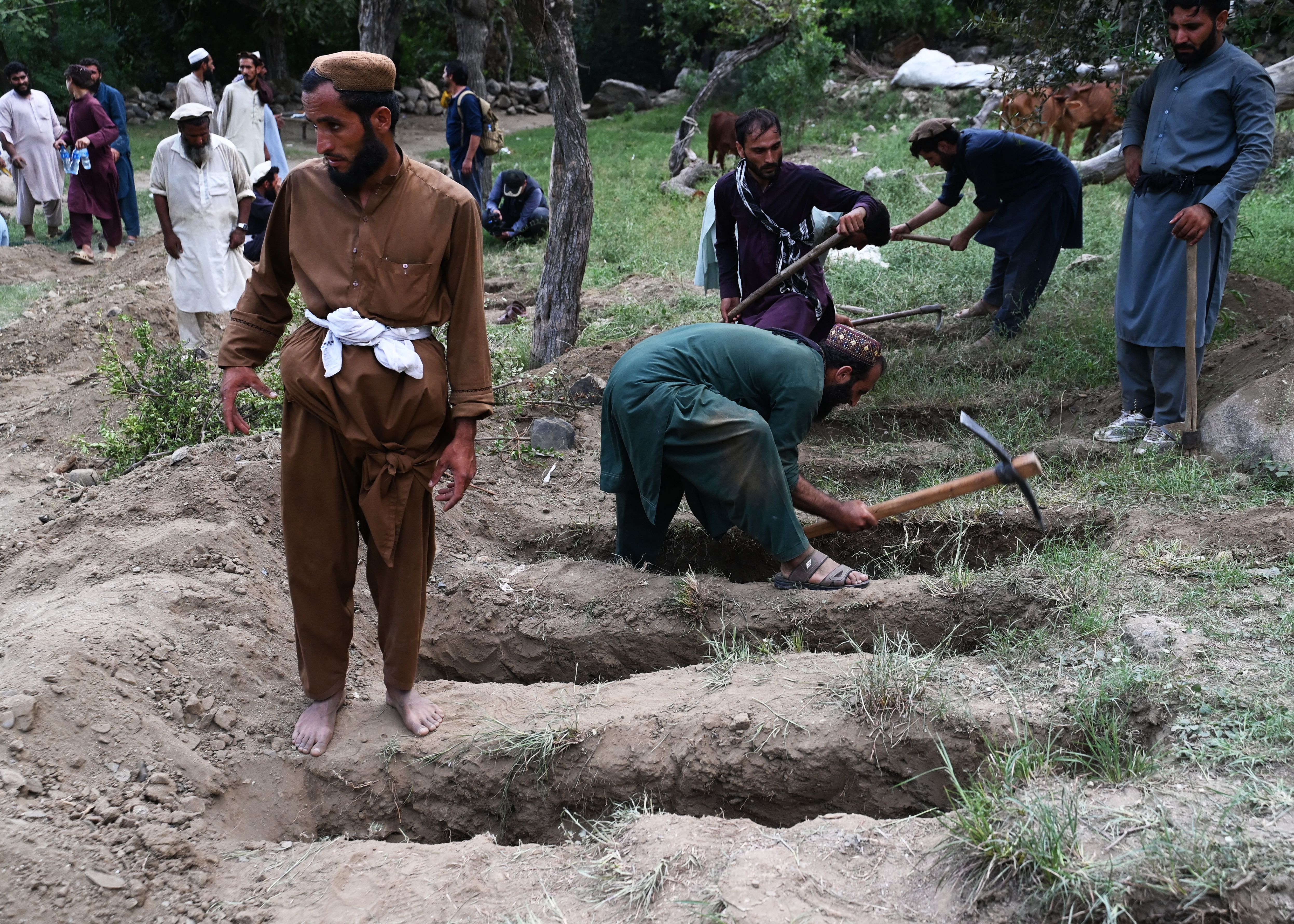 Men in traditional Afghan dress dig graves in the grass.