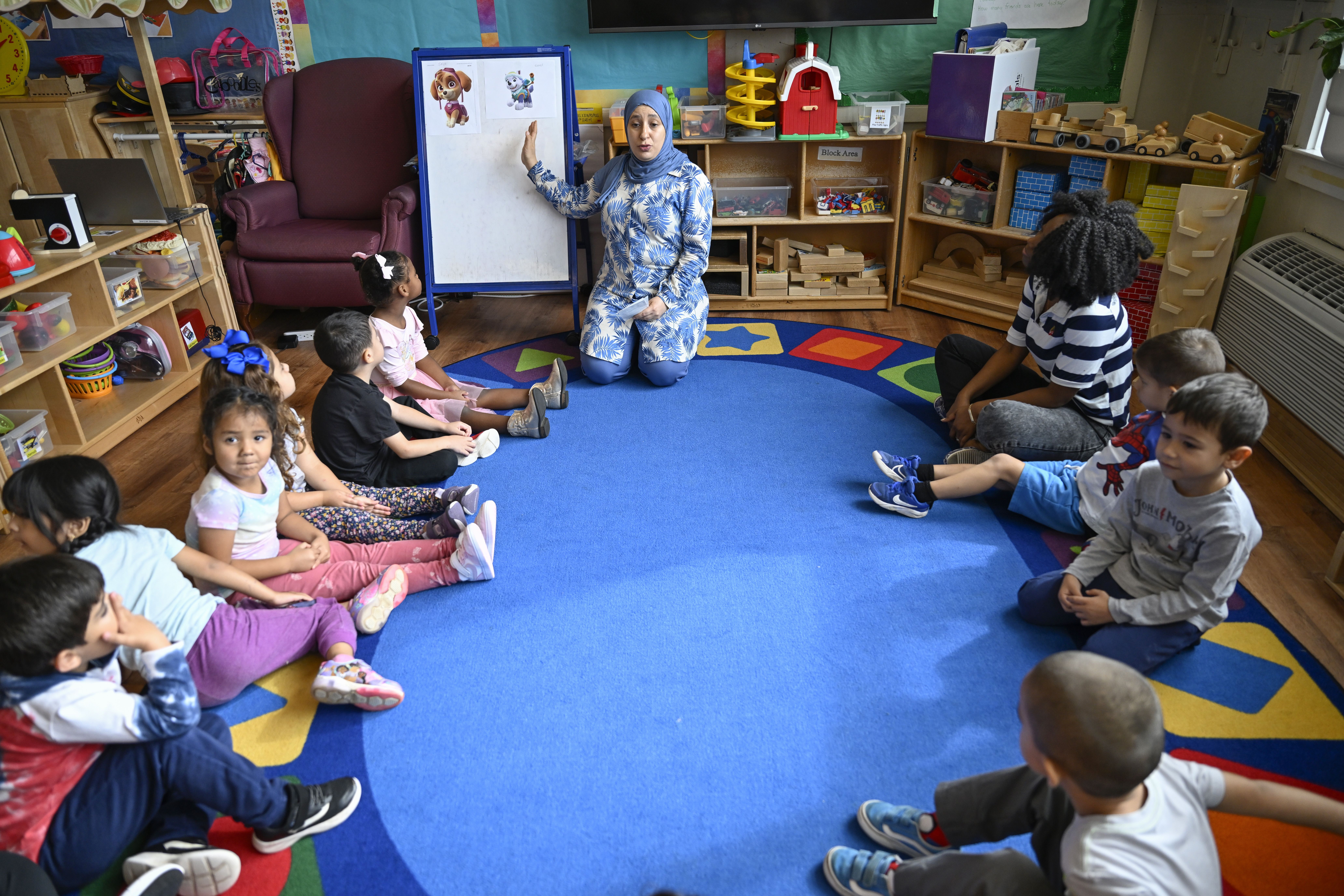 Kids sit around a rug looking at a board with cartoon dogs on it