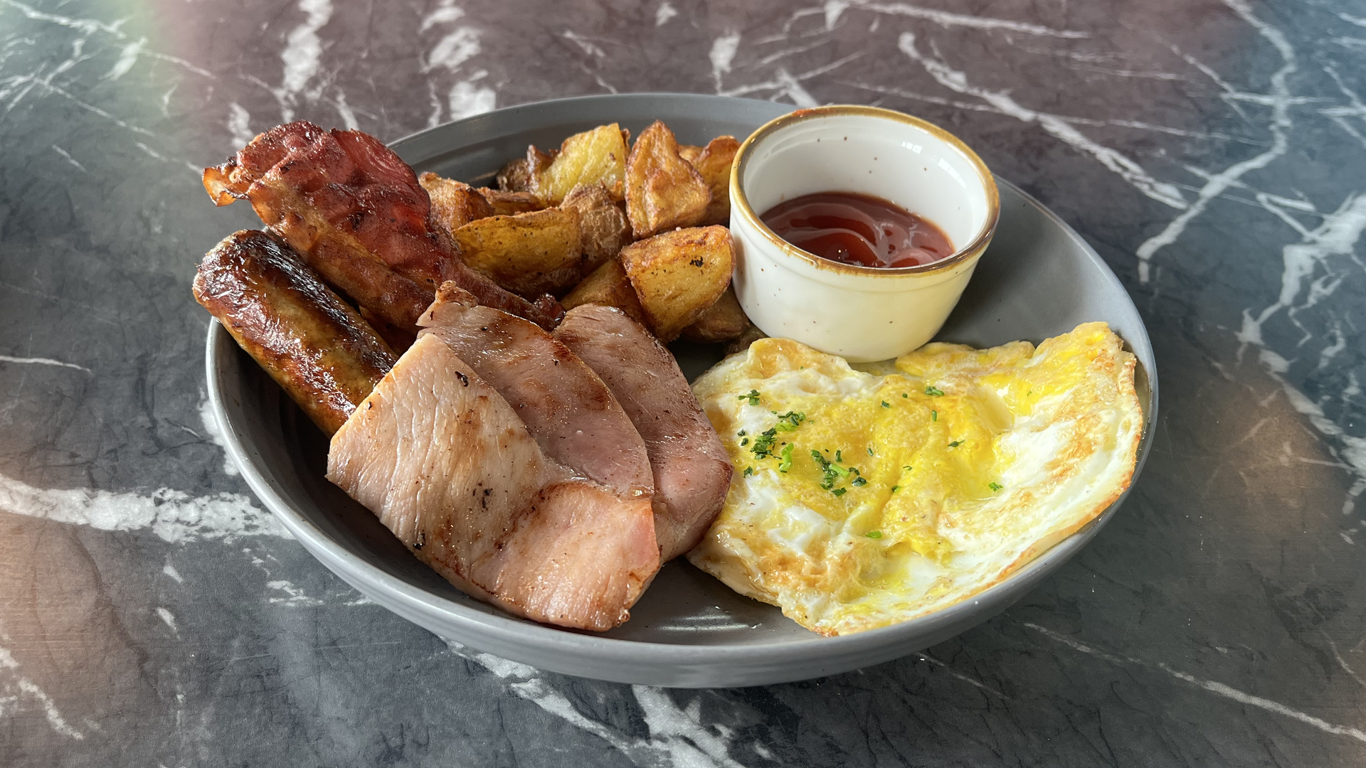 A breakfast plate with eggs, sausage, bacon, ham and potatoes.
