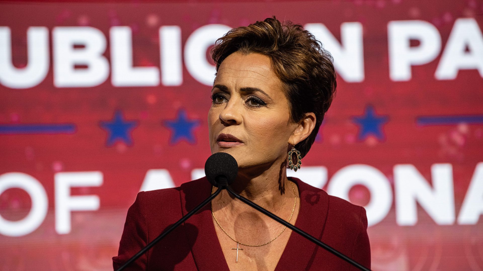 A woman speaks into a microphone in front of a large red screen with the words Republican Party of Arizona on it. 