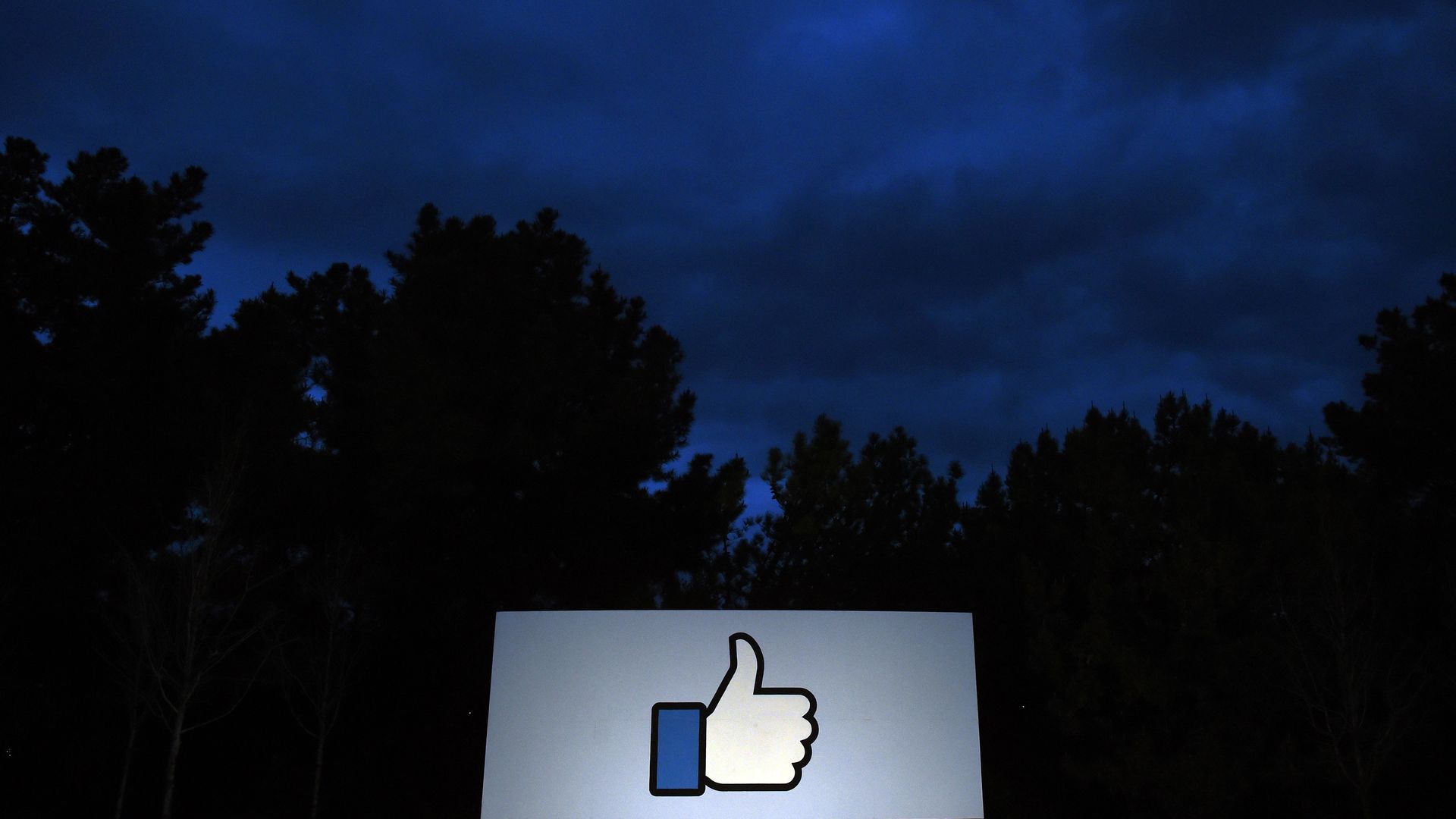 The Facebook "thumbs up" sign outside its office framed against a night sky