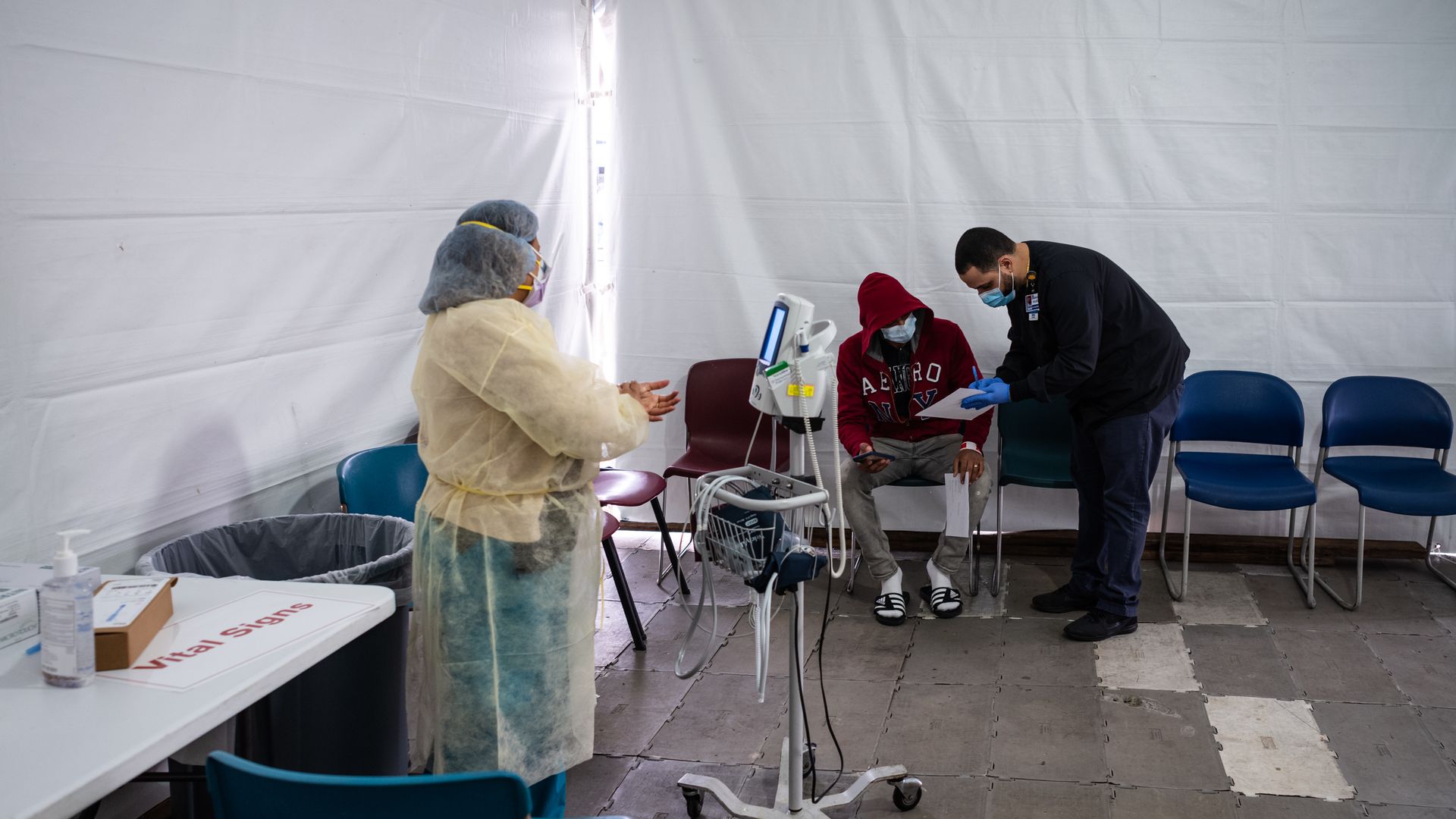 Clinicians prepare to test a patient for coronavirus inside a white tent.