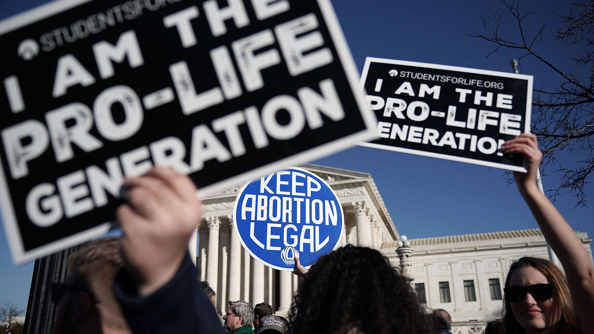 Pro-life activists hold up signs in front of a pro-choice activist.