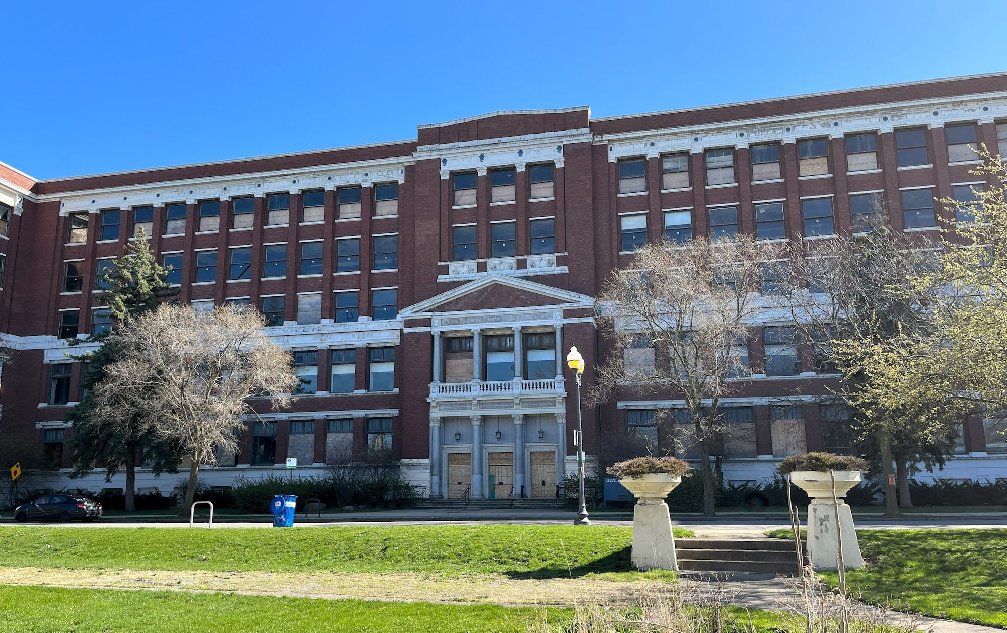 Large brown brick and white building with boarded doors.