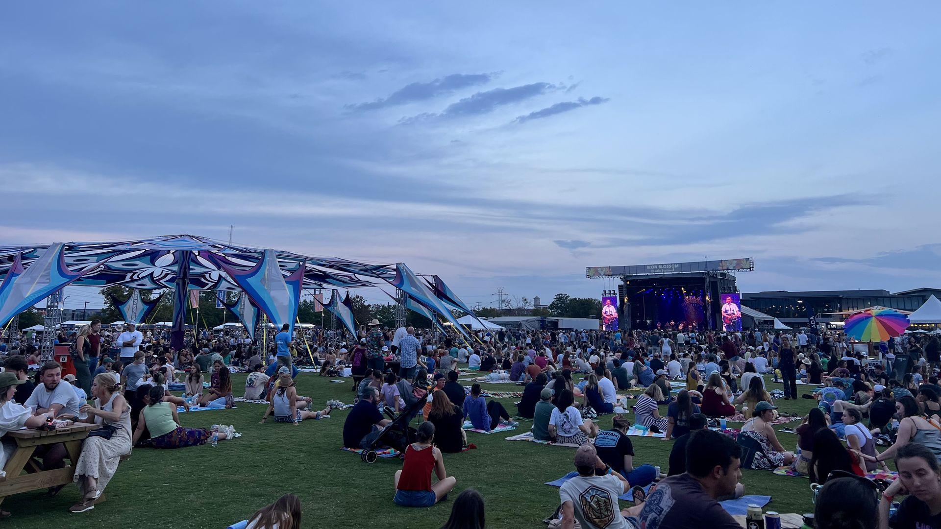 A crowd of people laying on a turn field on blankets while a stage is farther in front of them.