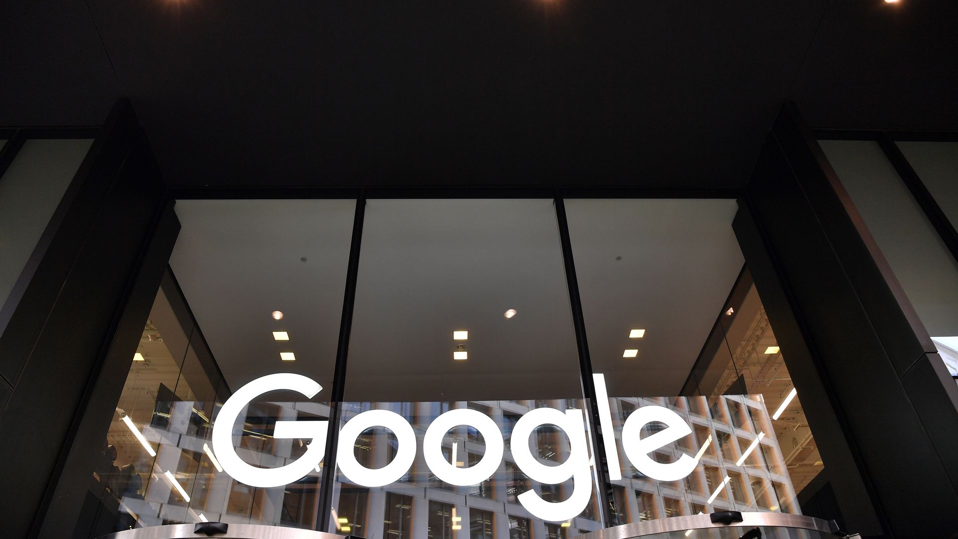 In this image, the white Google logo is seen at the bottom of three large glass windows on the side of a building. 