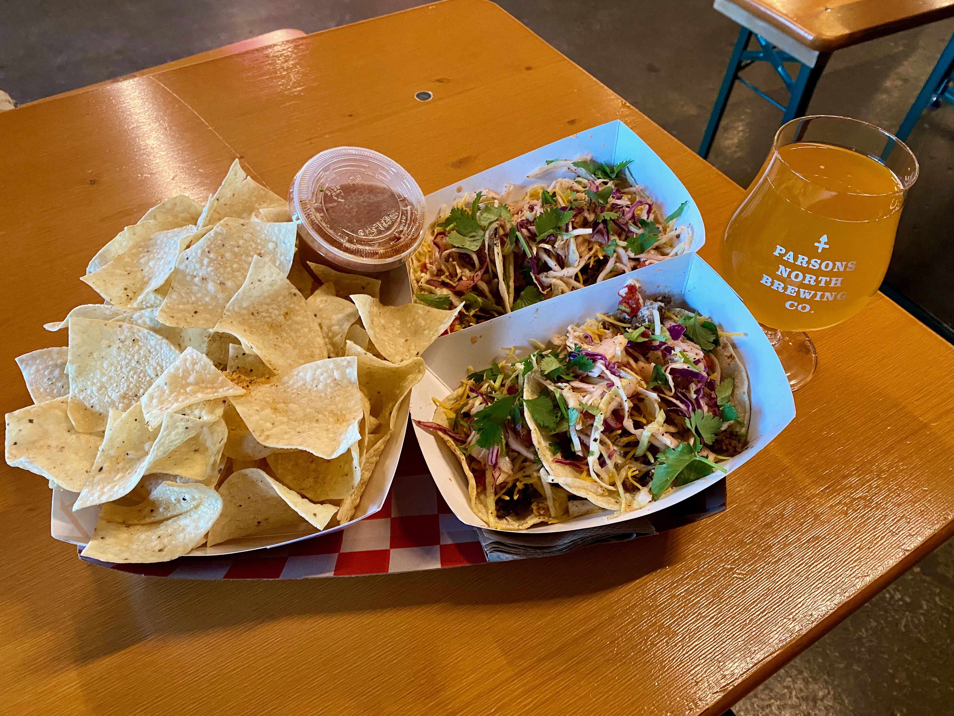 Three tacos, chips and salsa and a beer glass. 