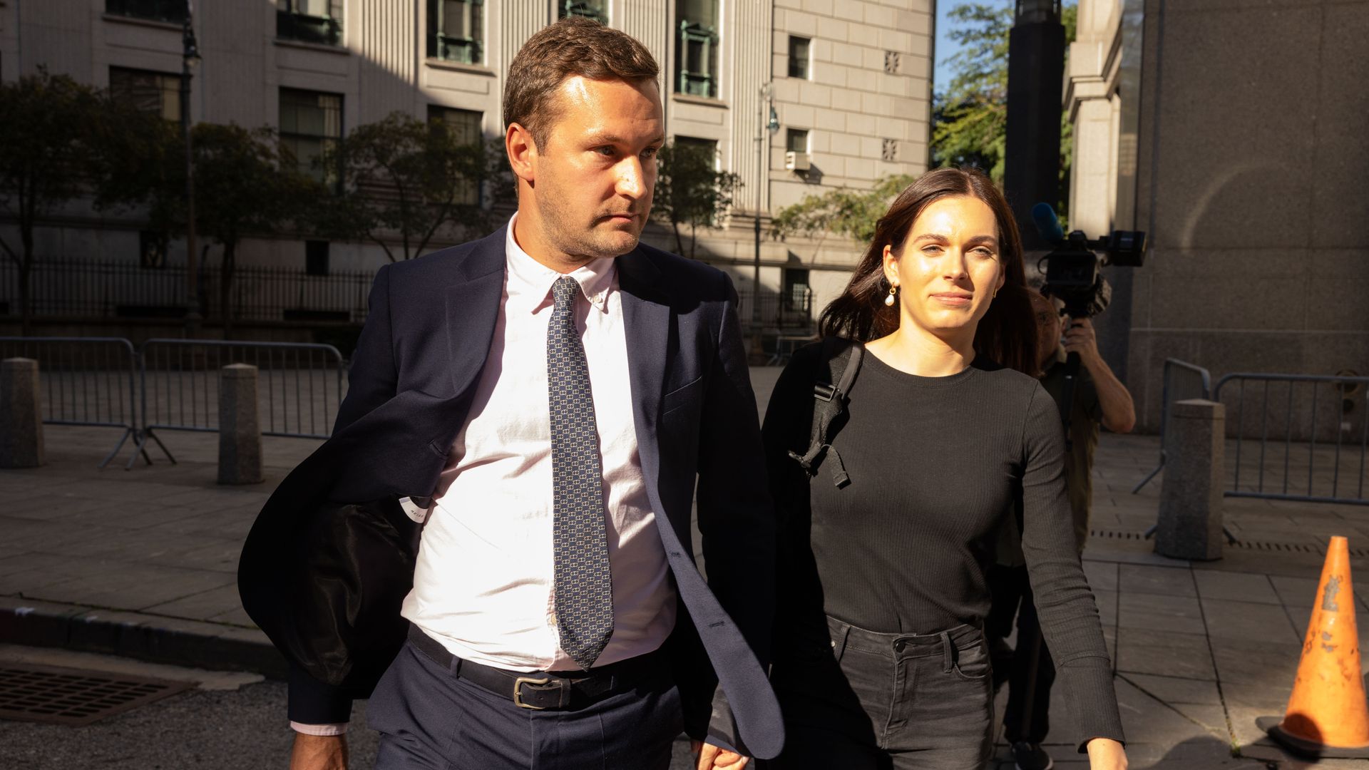 A man and woman walk quickly, seemingly distracted my cameras.