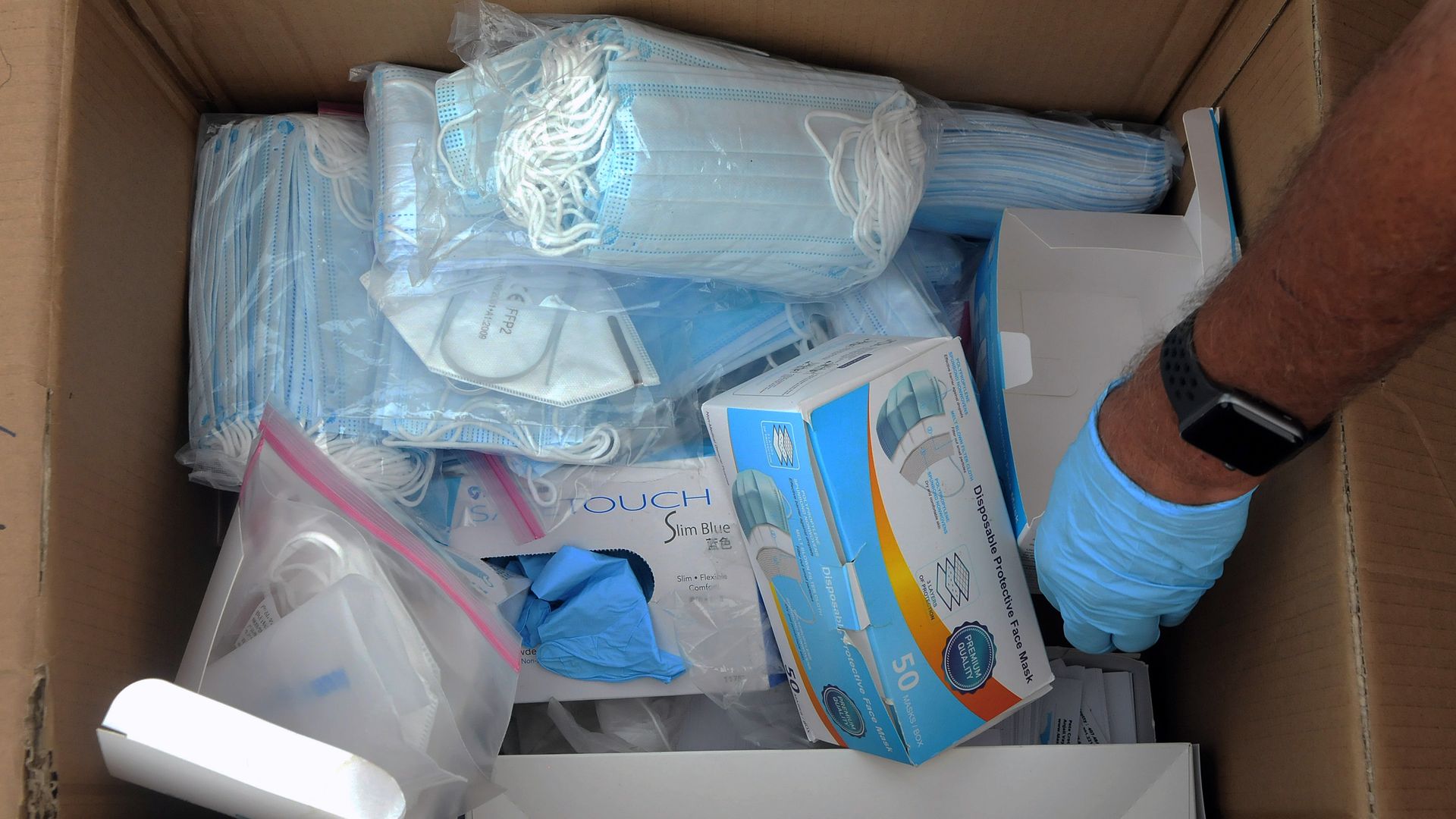 Photo of an arm reaching into a box of surgical face masks