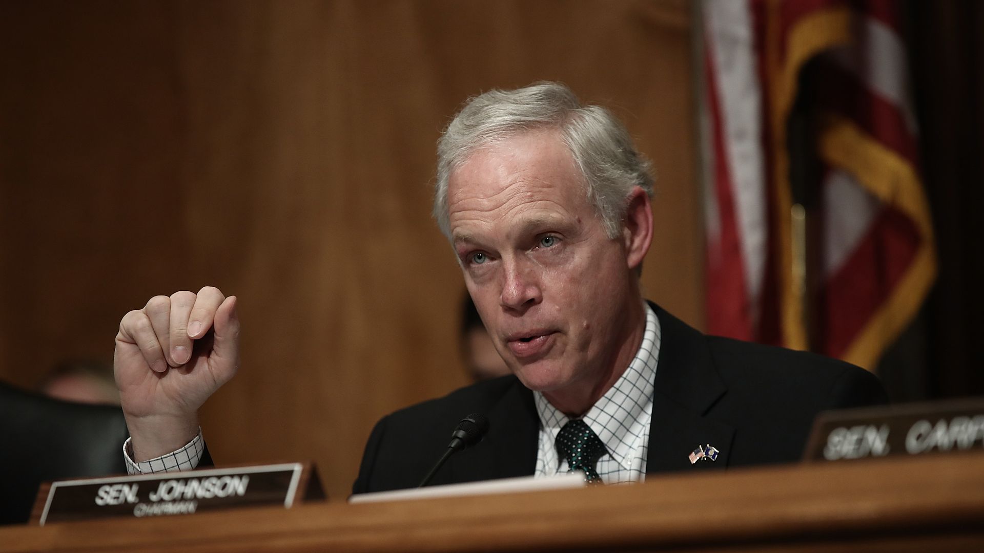 Senator Ron Johnson sits in front of his nameplate on a dais.