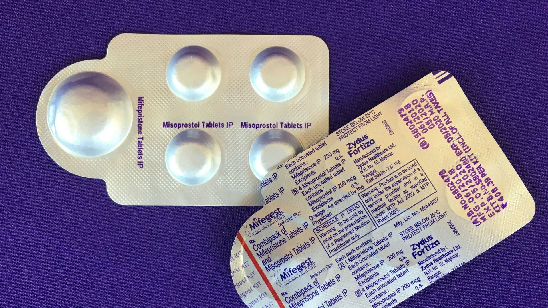 Two silver packs of pills with five pills each on a purple background.