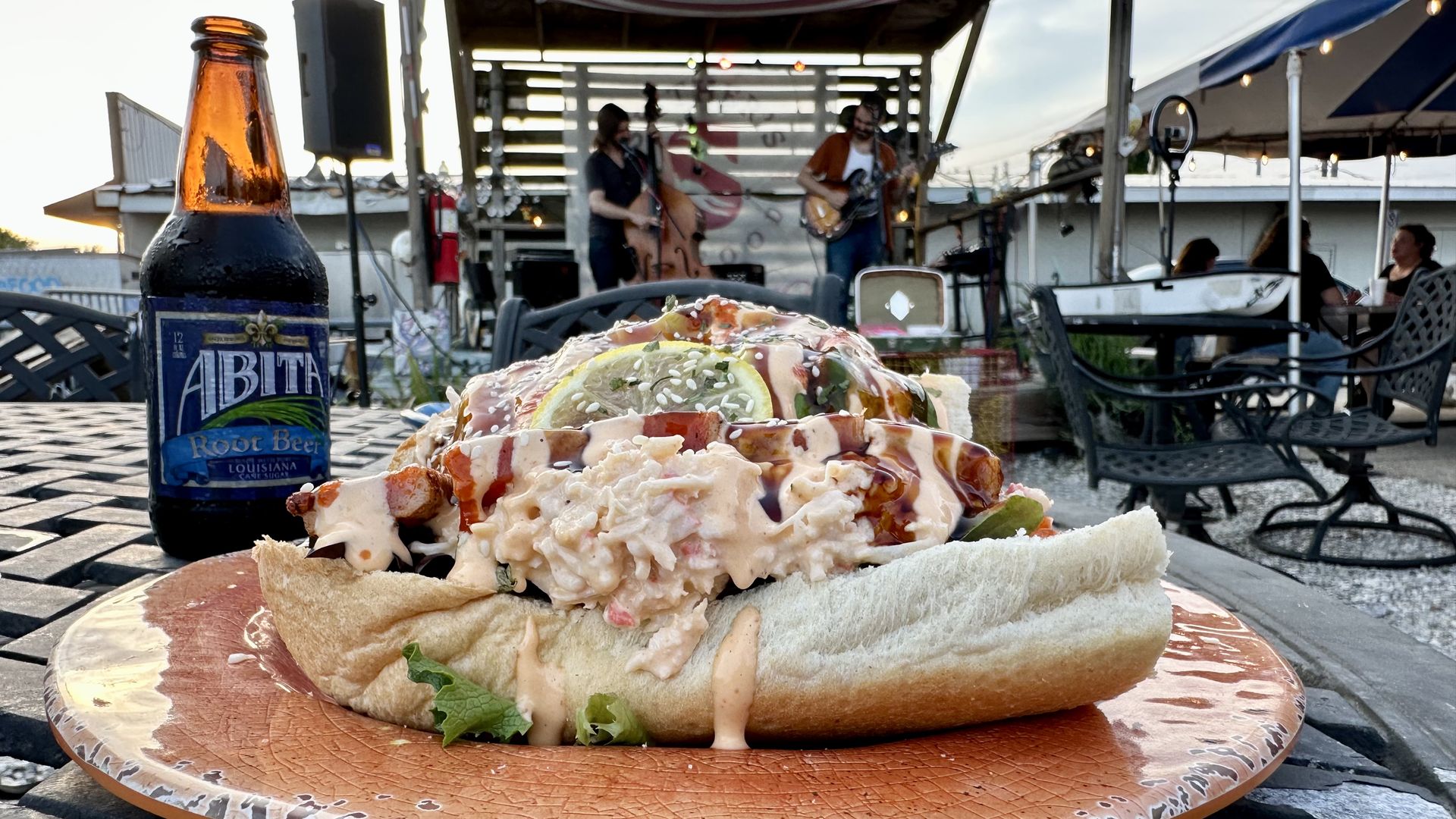 Photo shows a poboy piled with crab salad and sauces on a reddish plate.