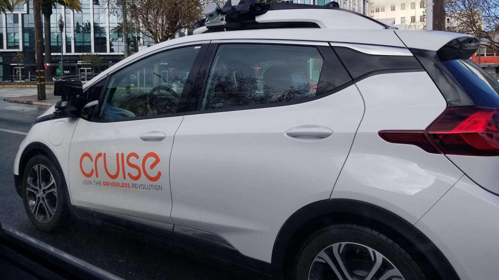 In this image, a driverless car with a Cruise logo drives down the street.