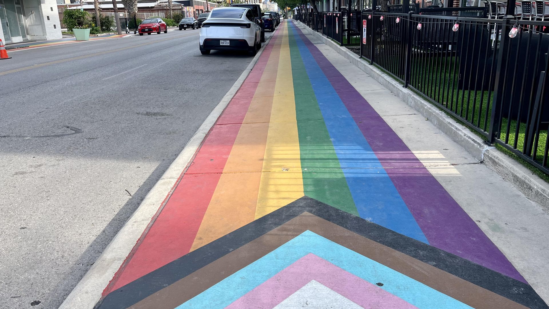 The sidewalk along Main Avenue in San Antonio is decorated with rainbow lines and an arrow with white, pink, light blue, brown and black lines. The arrow represents the transgender communities and communities of color.