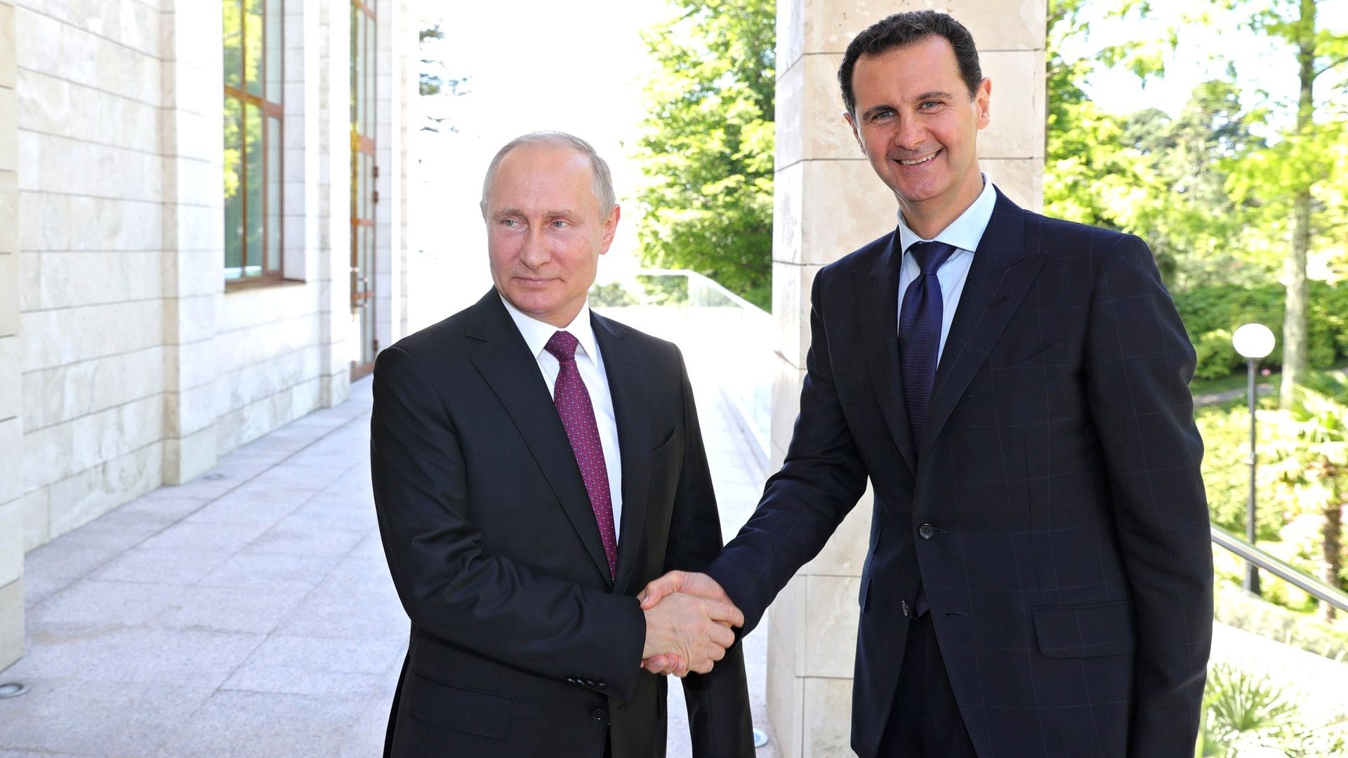 Vladimir Putin and Bashar al-Assad shaking hands and smiling