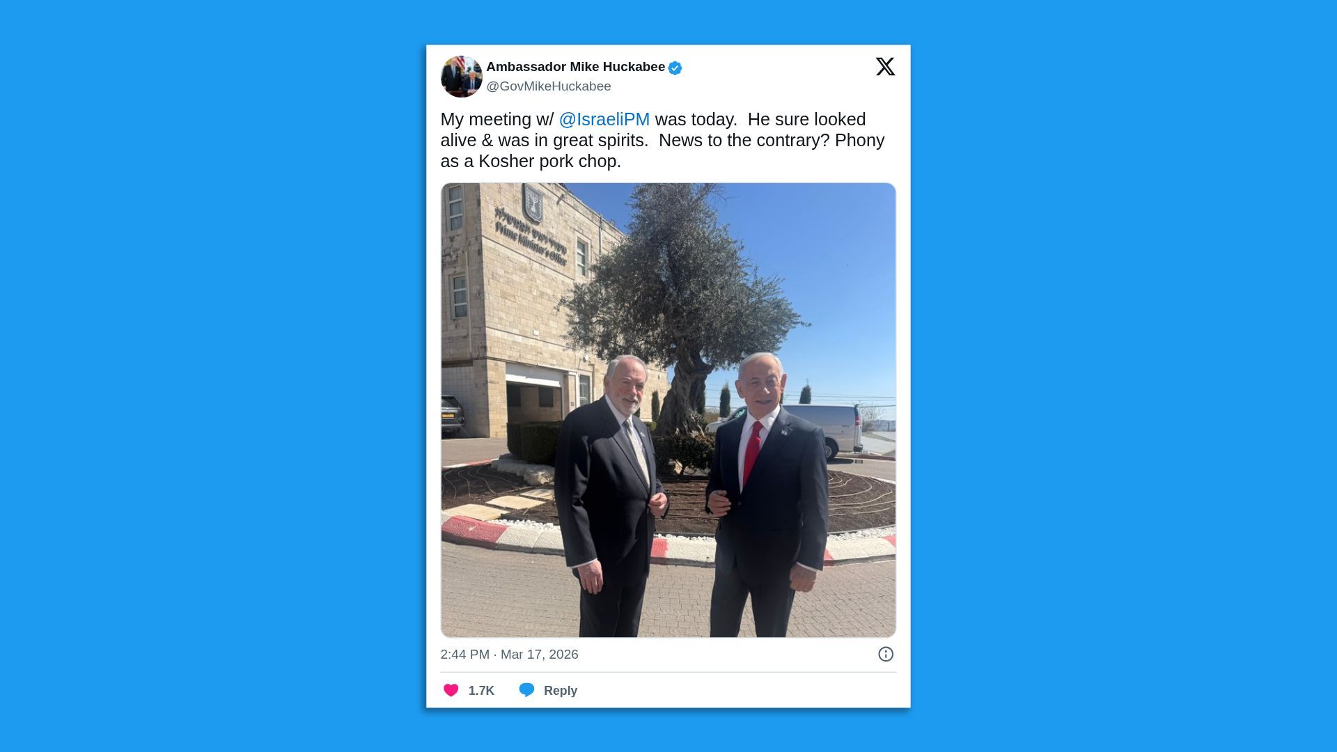 Screenshot of a tweet showing two suited men standing outdoors in front of a building and tree.