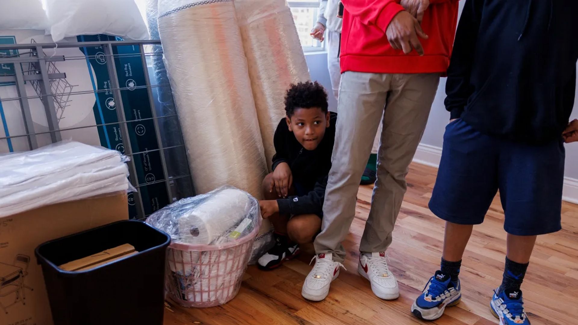 Little boy kneeling before an adult's legs, next to a filled laundry baskey.