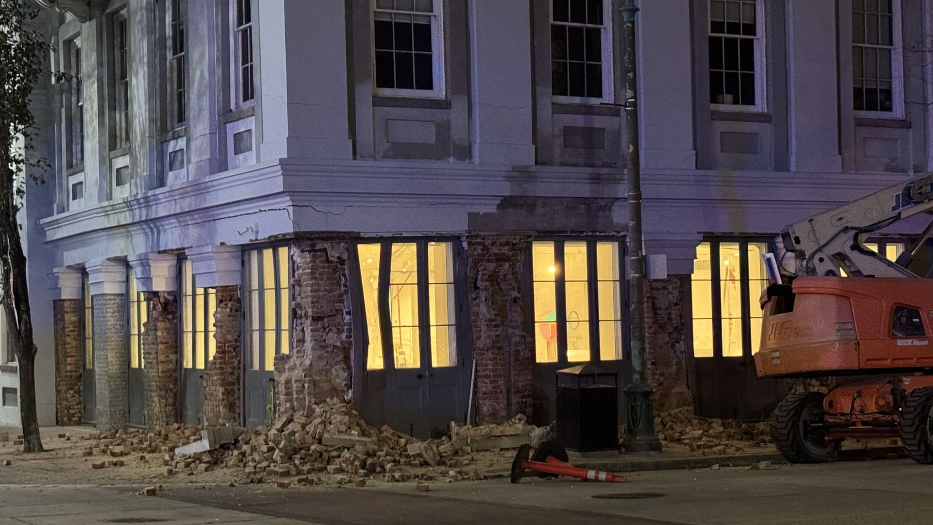 The brick facade of a building is crumbled apart on a sidewalk.